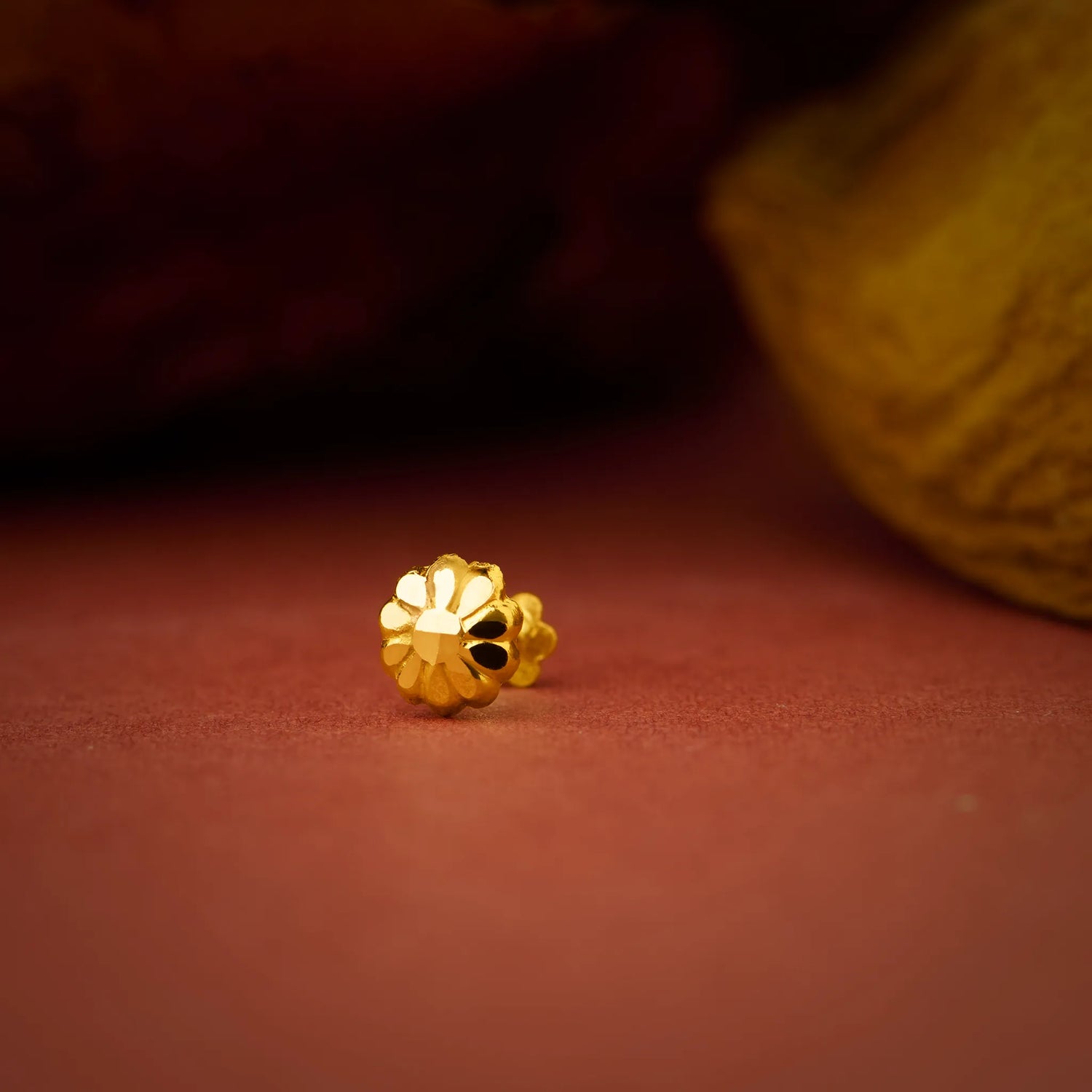 Close up of small flower inspired 18K gold nose pin placed on a warm terracotta background with soft shadows