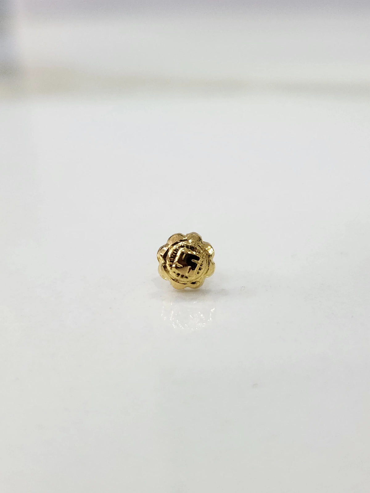 Close-up of tiny Swastik Bloom 18K Nose Pin Gold on white marble background displaying textured swastik design