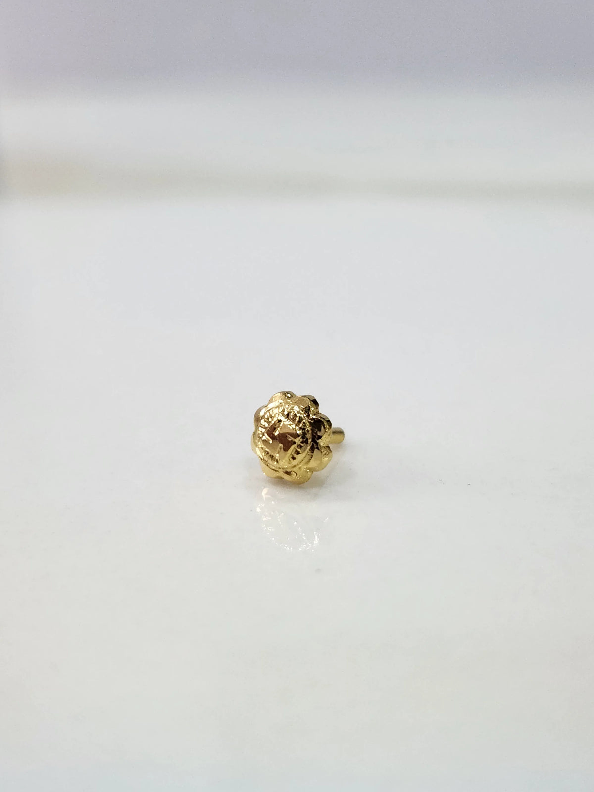Small Swastik Bloom 18K Nose Pin Gold placed on white surface showing intricate floral detailing
