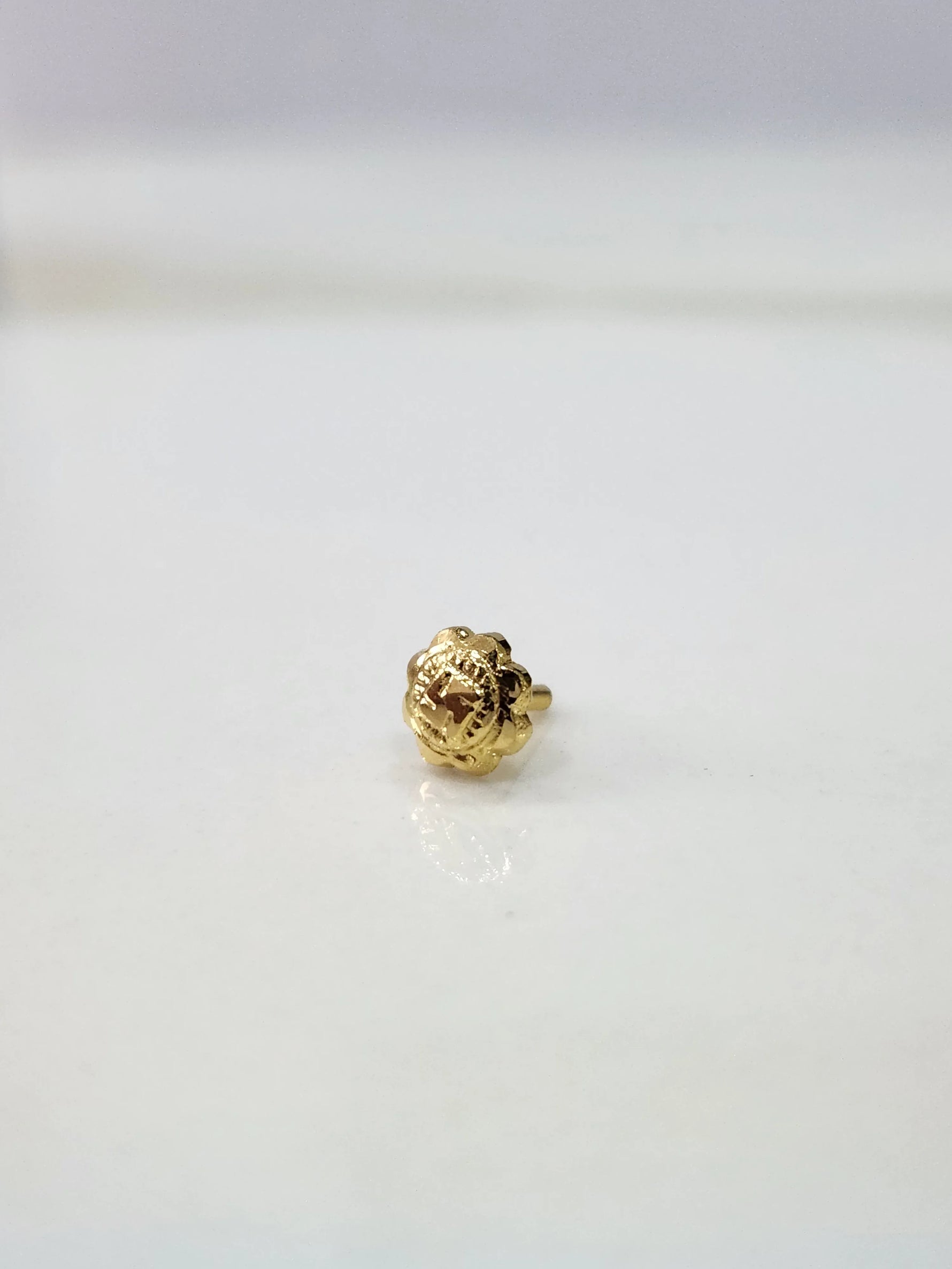 Small Swastik Bloom 18K Nose Pin Gold placed on white surface showing intricate floral detailing