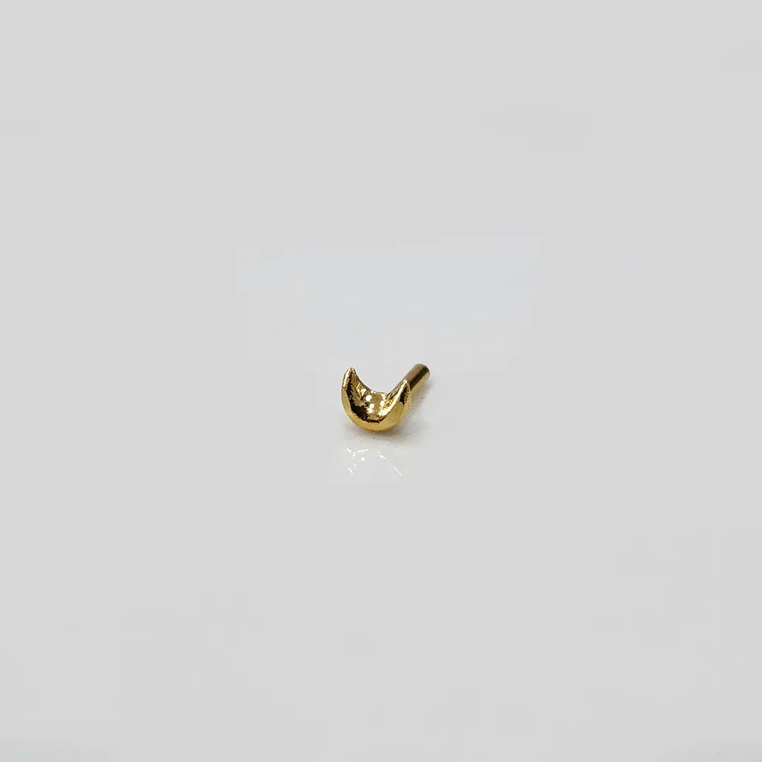 Close up of crescent gold nose pin on white surface highlighting polished shine and smooth edges
