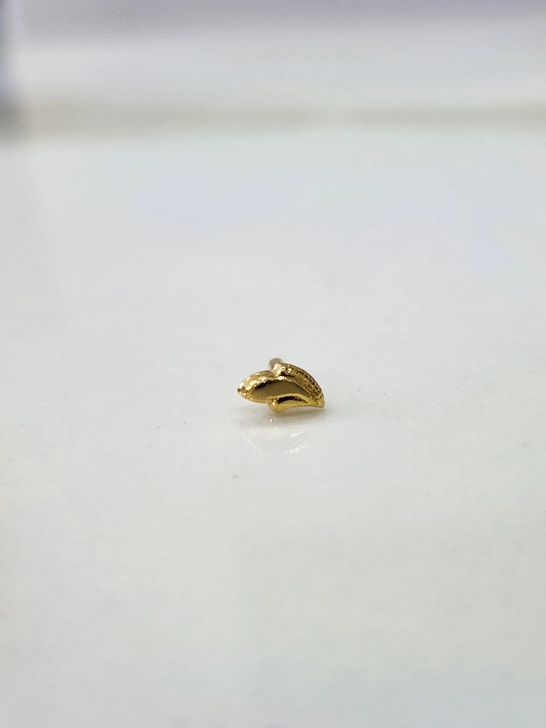 Side view of a tiny gold nose pin on a white surface highlighting its fine detailing