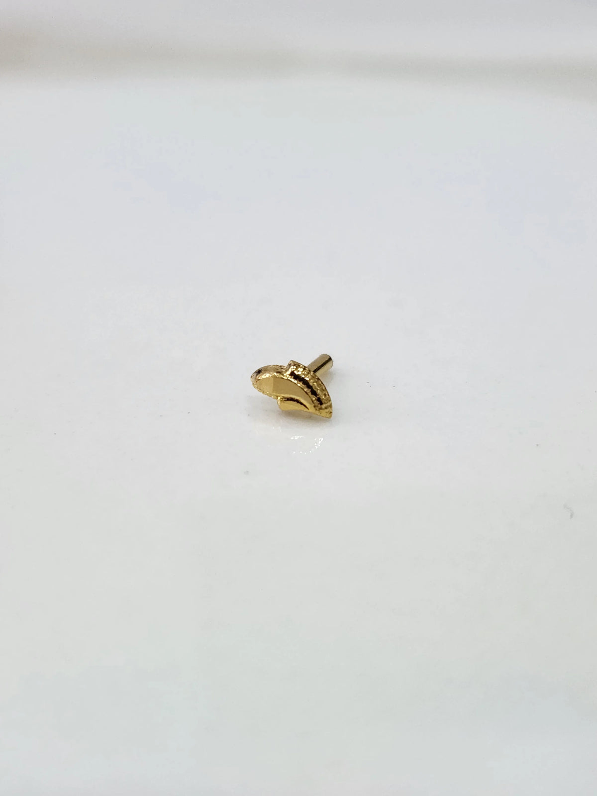 Front view of a small gold nose pin placed on a white background showing its compact size