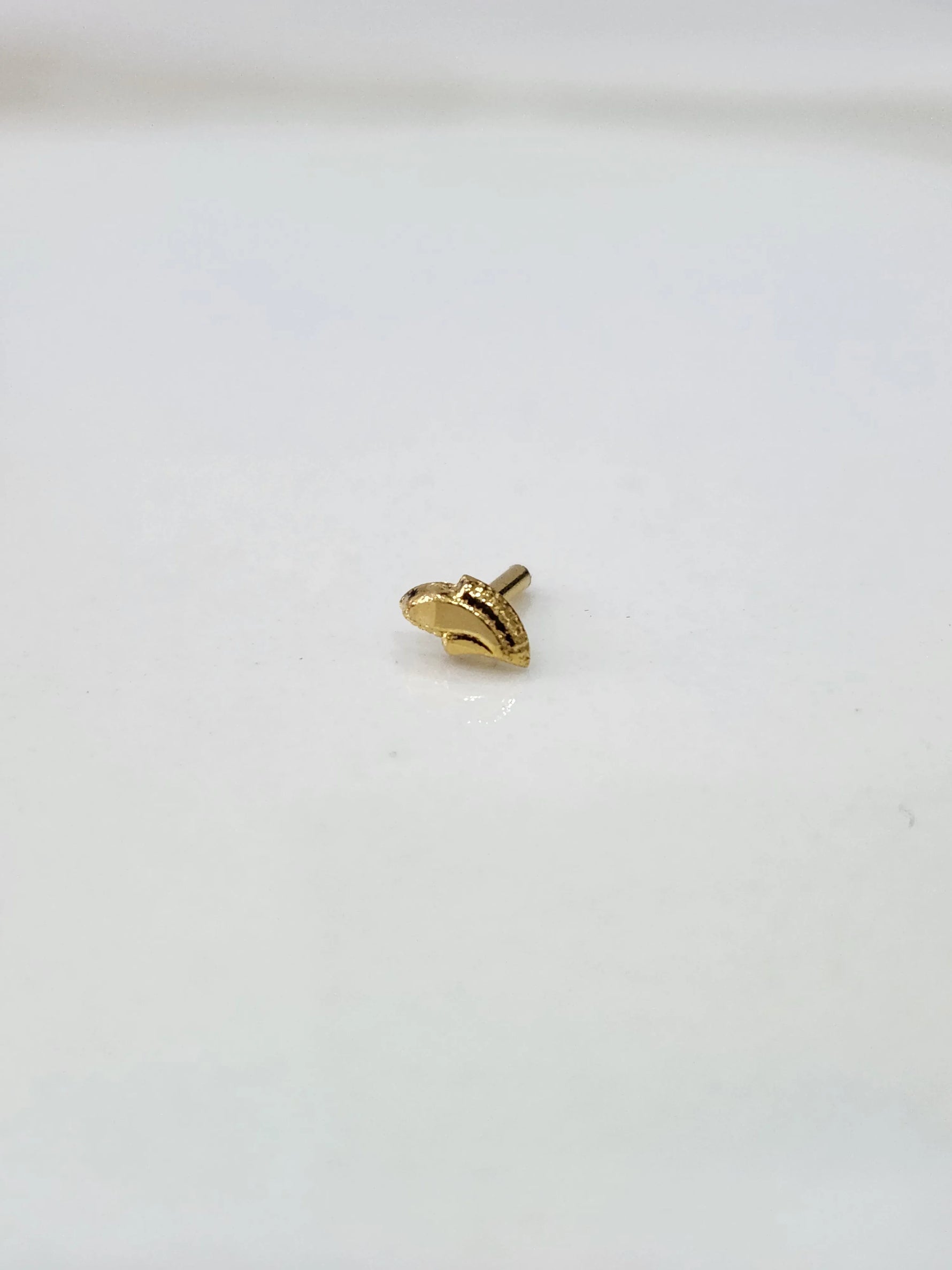 Front view of a small gold nose pin placed on a white background showing its compact size