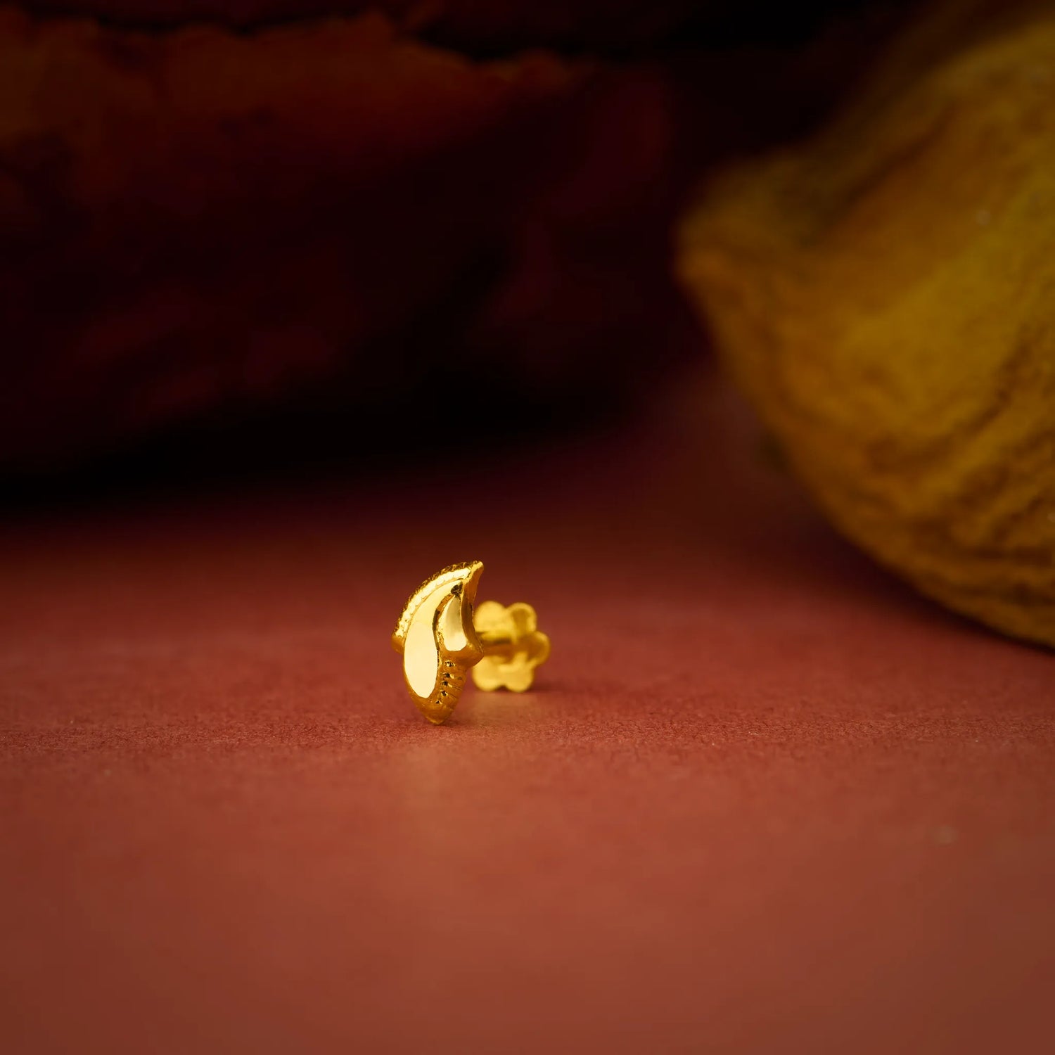 Close up of a crescent style gold nose pin placed on a warm textured surface highlighting its smooth shine
