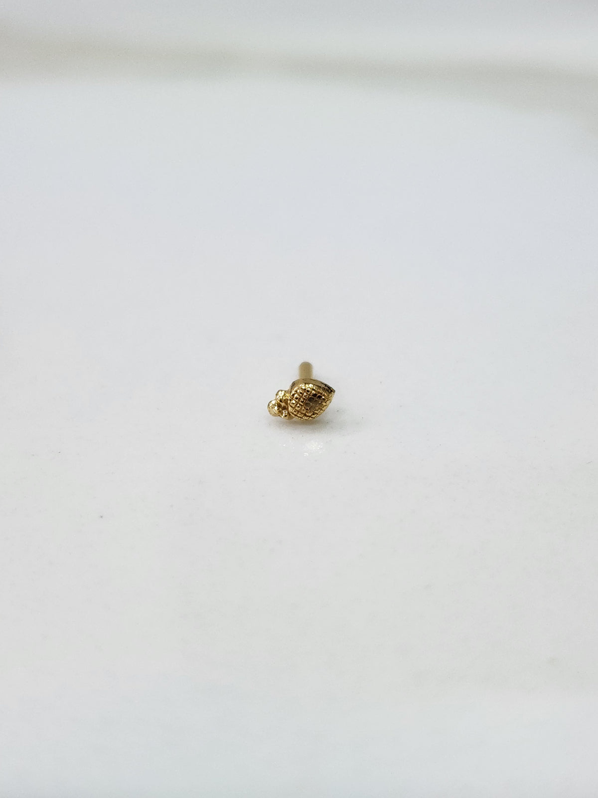 Side angle view of a small gold nose pin on a white surface highlighting its fine detailing and shape