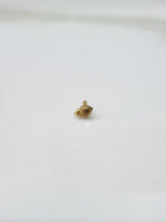 Side angle view of a small gold nose pin on a white surface highlighting its fine detailing and shape