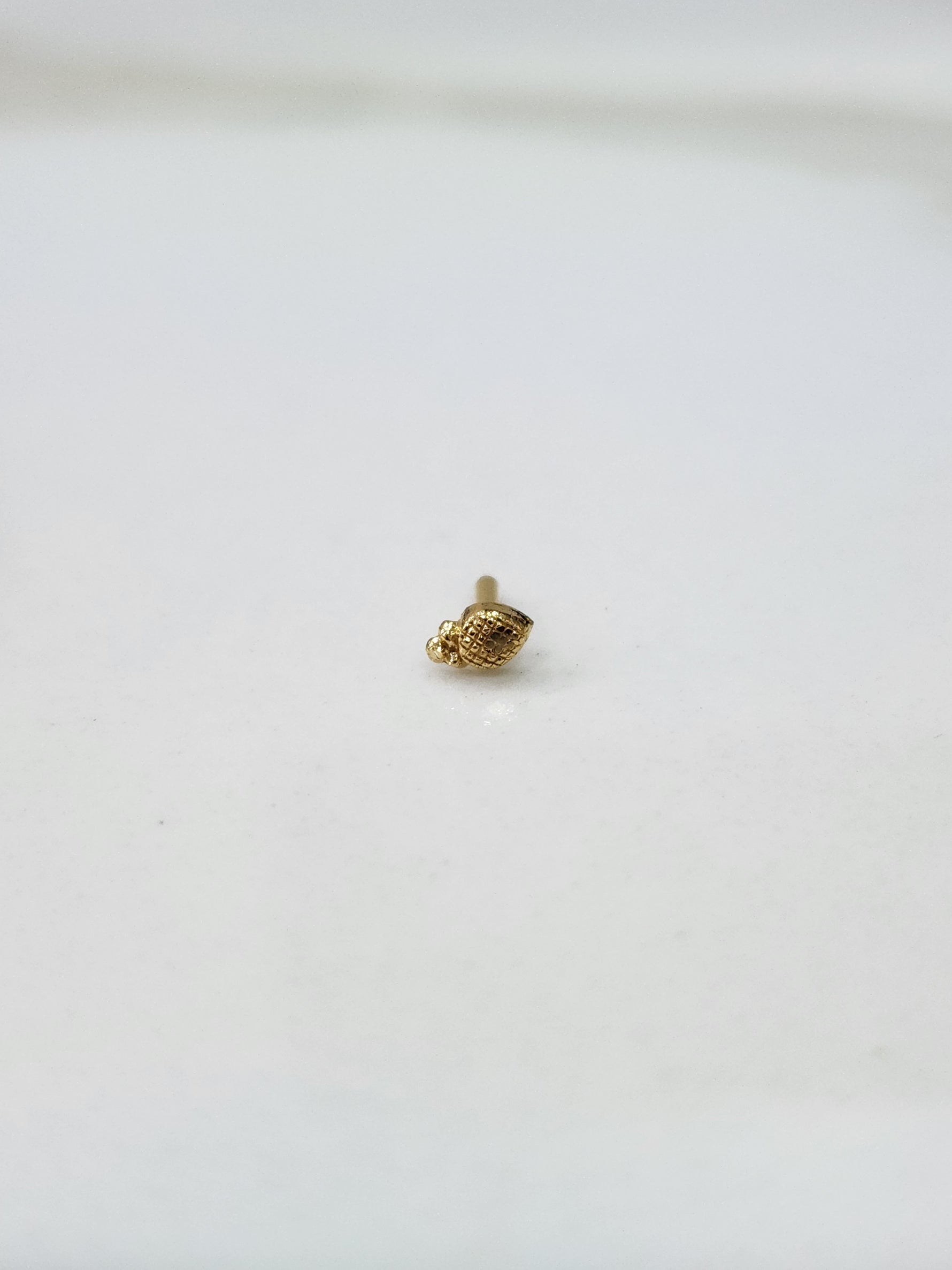 Side angle view of a small gold nose pin on a white surface highlighting its fine detailing and shape