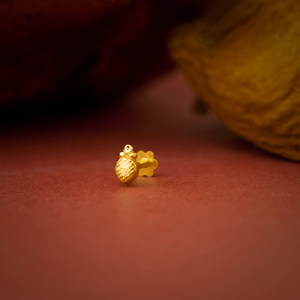Close up of a small gold nose pin placed on a warm brown textured surface highlighting its smooth polished finish