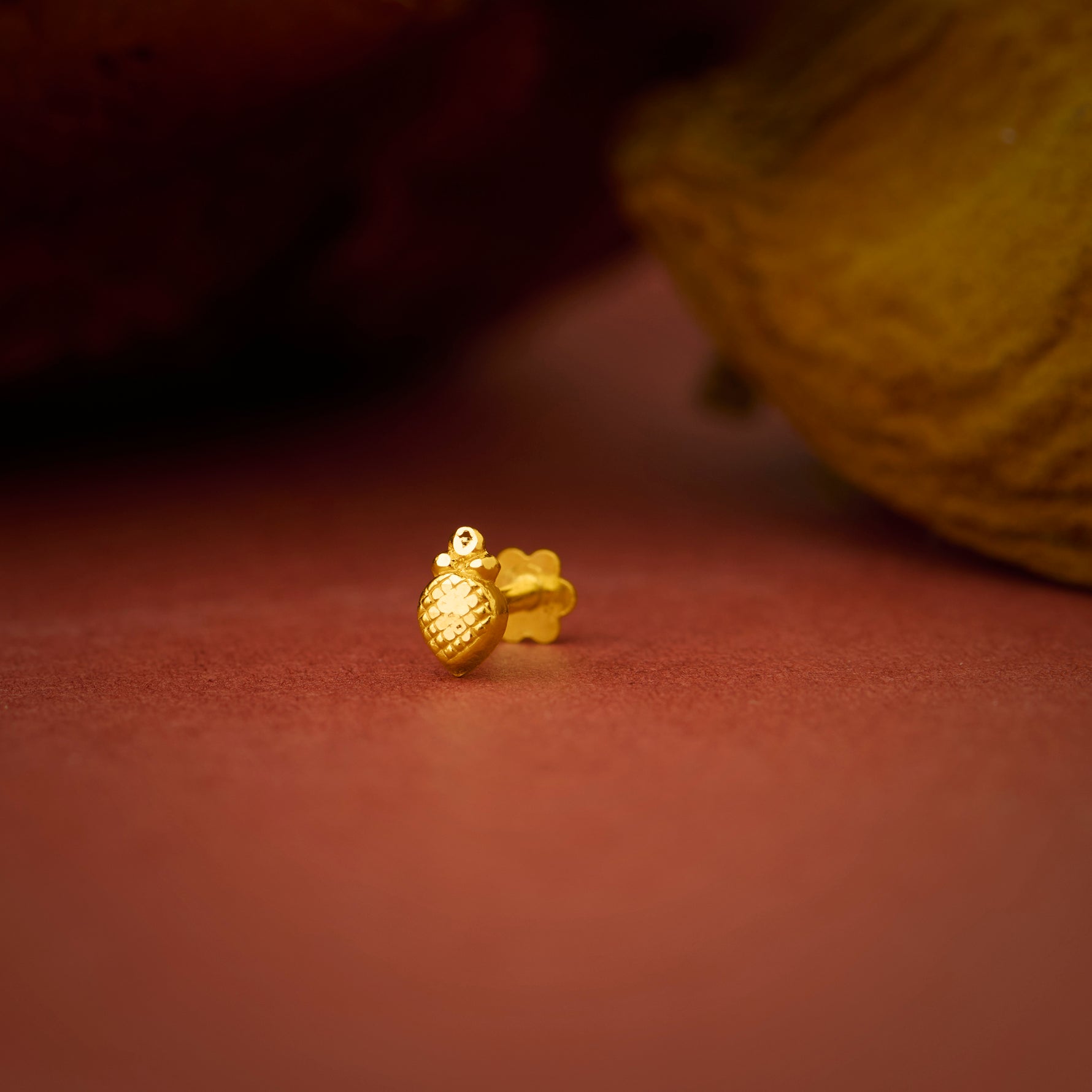 Close up of a small gold nose pin placed on a warm brown textured surface highlighting its smooth polished finish