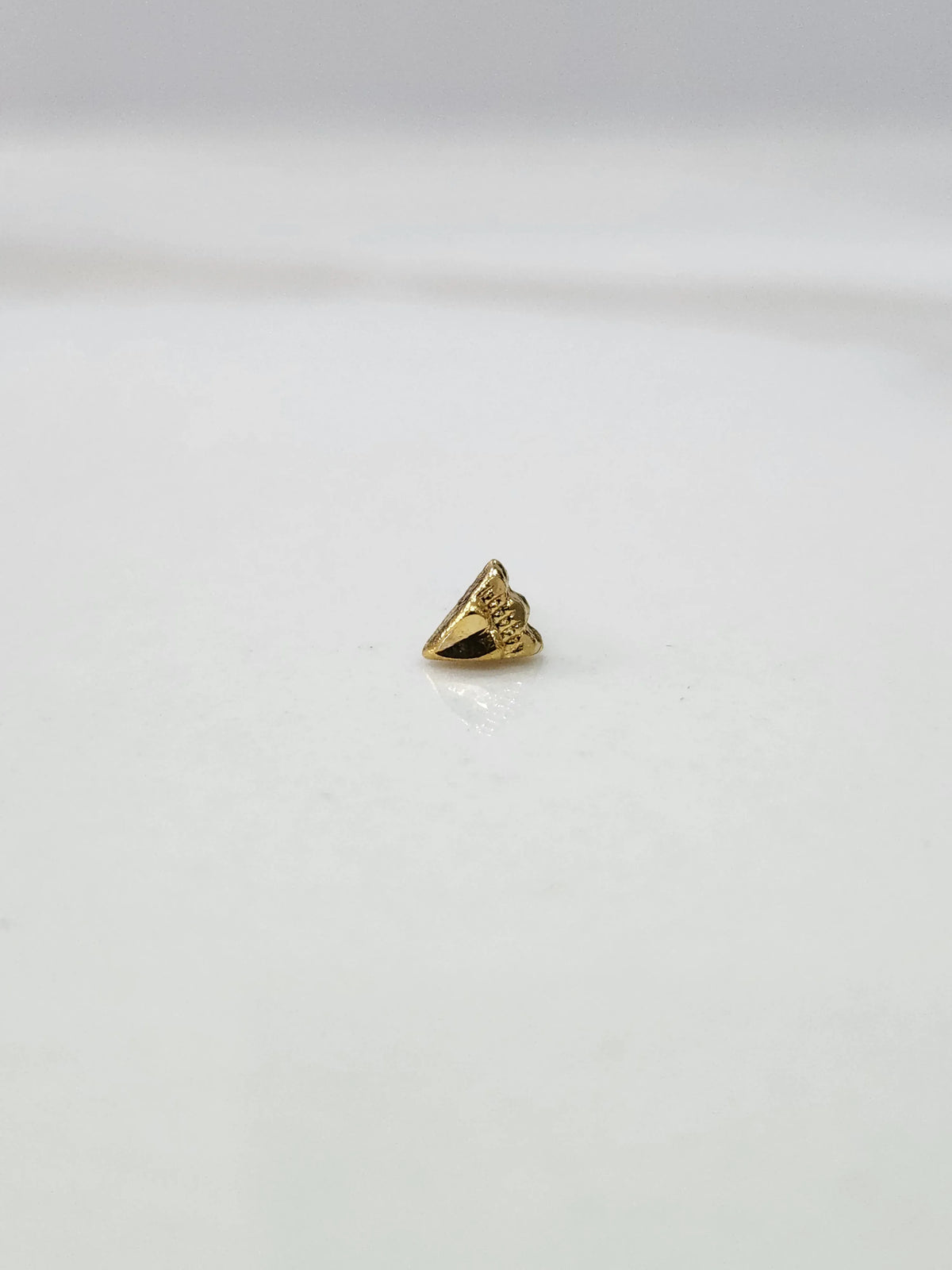 Side view of a tiny gold nose pin on a white surface highlighting its pointed design and subtle shine