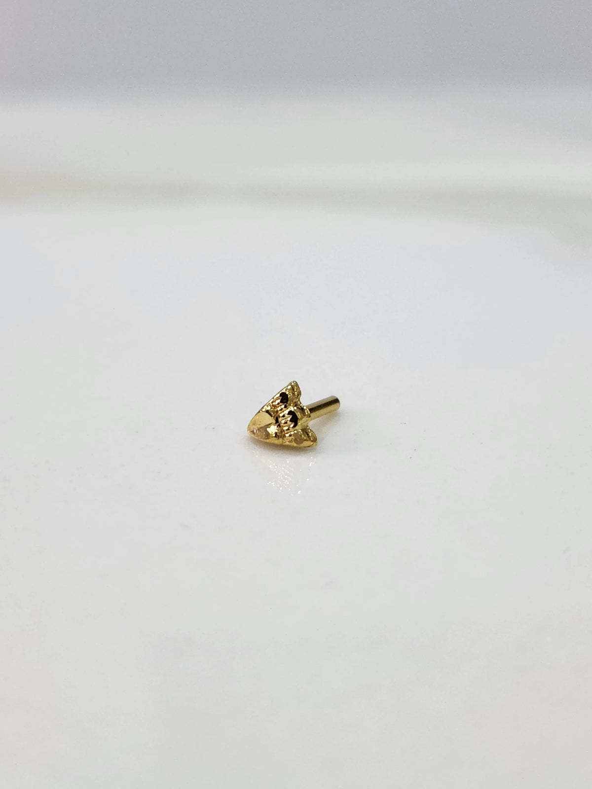 Small gold nose pin placed on a white background showing its compact size and clean detailing