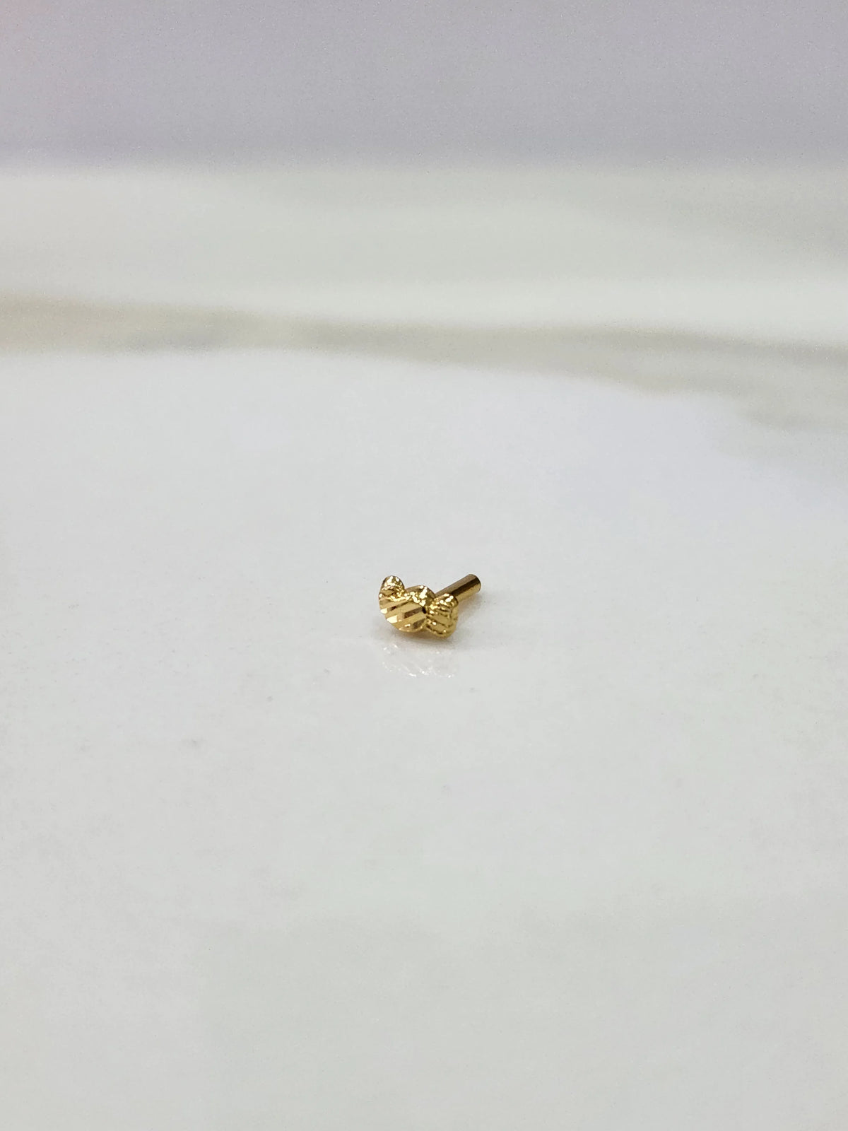 Side view of a delicate gold nose pin on a white surface highlighting its smooth edges and lightweight form