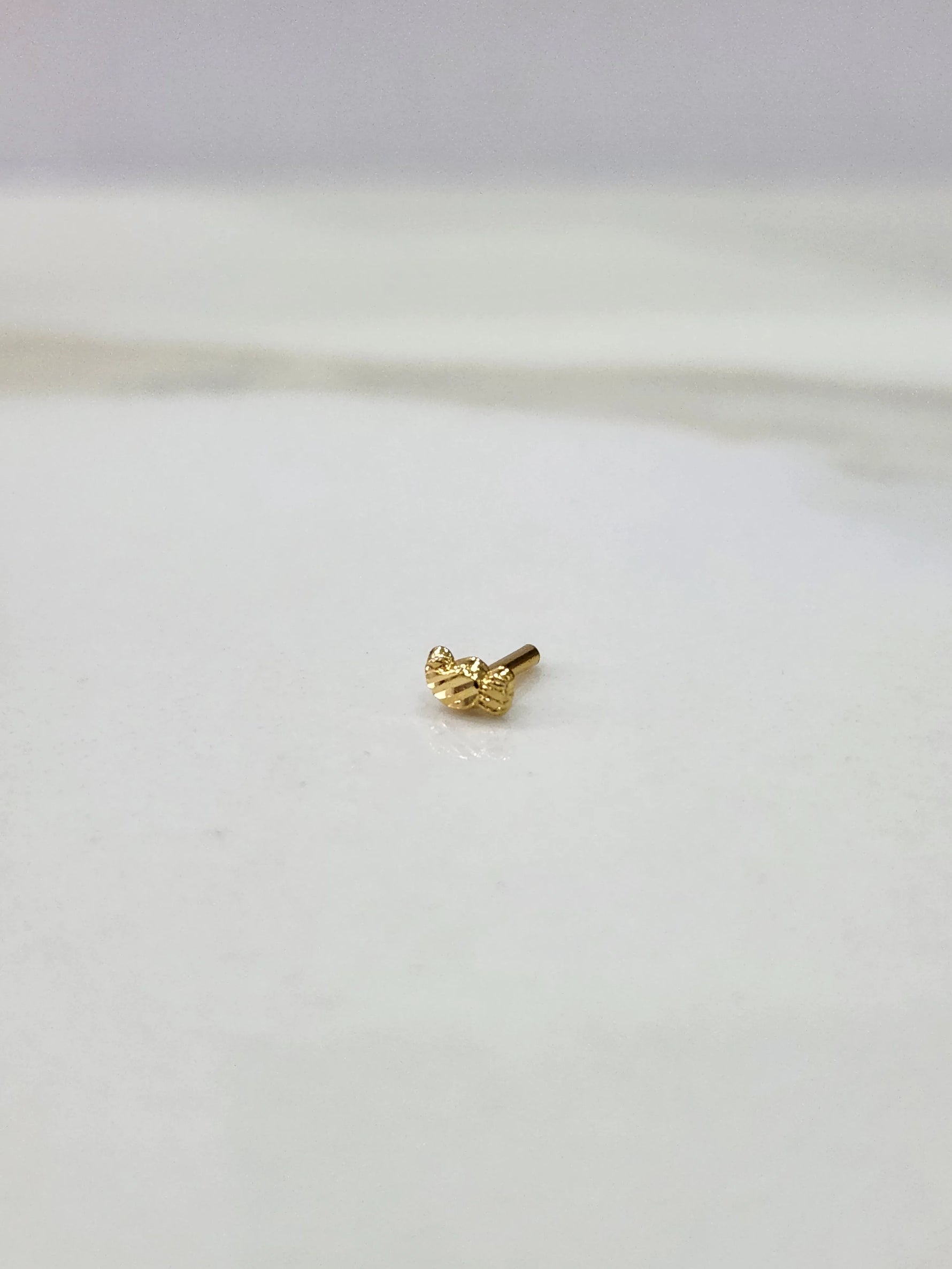 Side view of a delicate gold nose pin on a white surface highlighting its smooth edges and lightweight form
