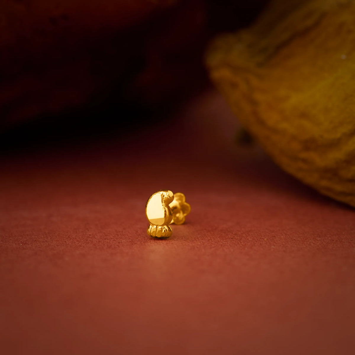 Close up of a small gold nose pin placed on a warm brown surface highlighting its polished finish and delicate design