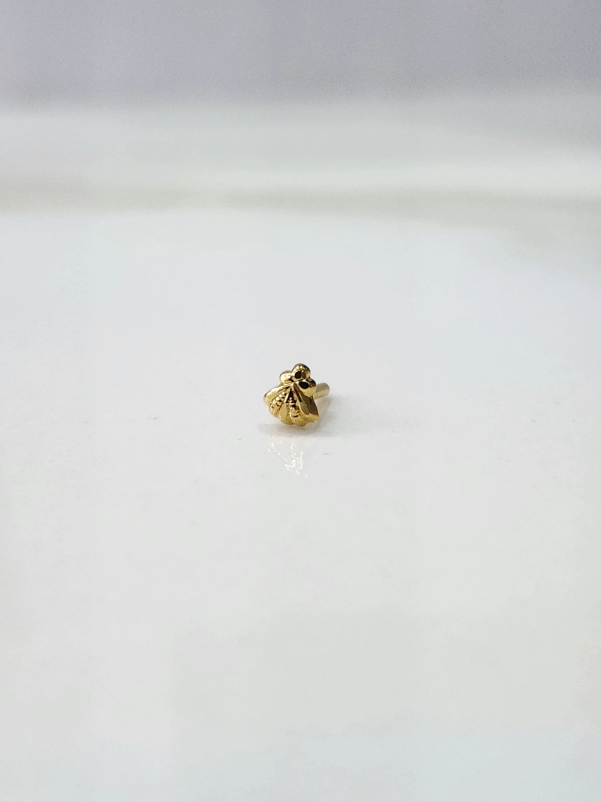 Side view of a delicate gold nose pin on a white surface highlighting its neat finish and lightweight form