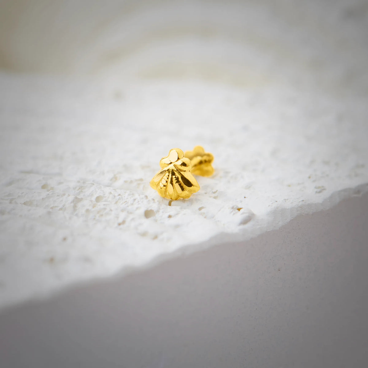 Close up of a gold nose pin placed on a textured white stone surface highlighting its smooth polish and compact design