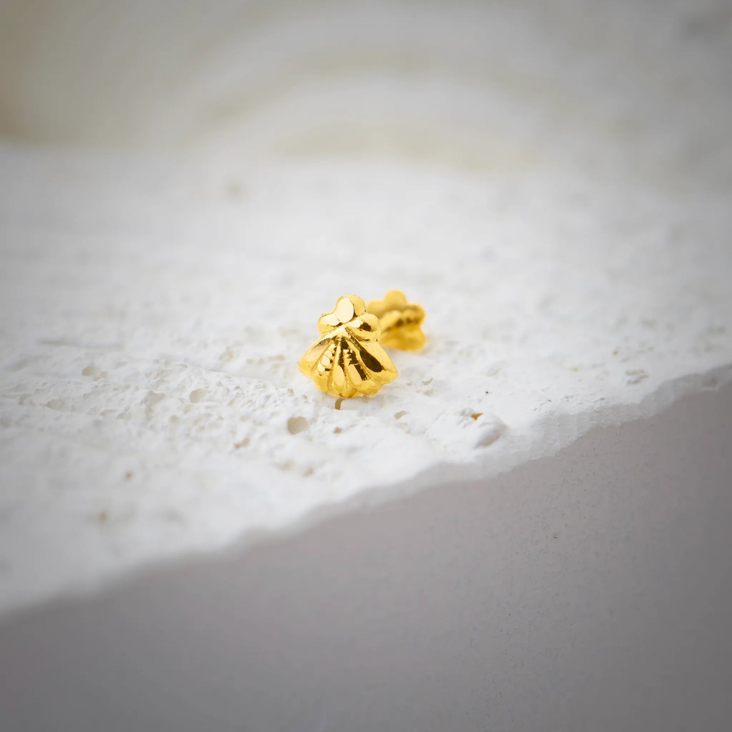 Close up of a gold nose pin placed on a textured white stone surface highlighting its smooth polish and compact design