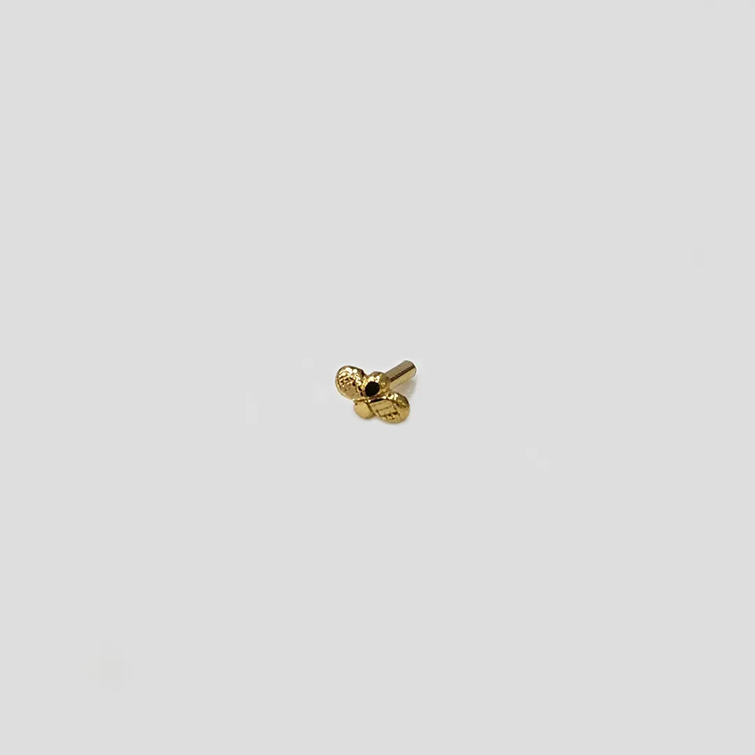 Close up of tiny twin knot design 18K gold nose pin on a light grey background showing minimalist detailing