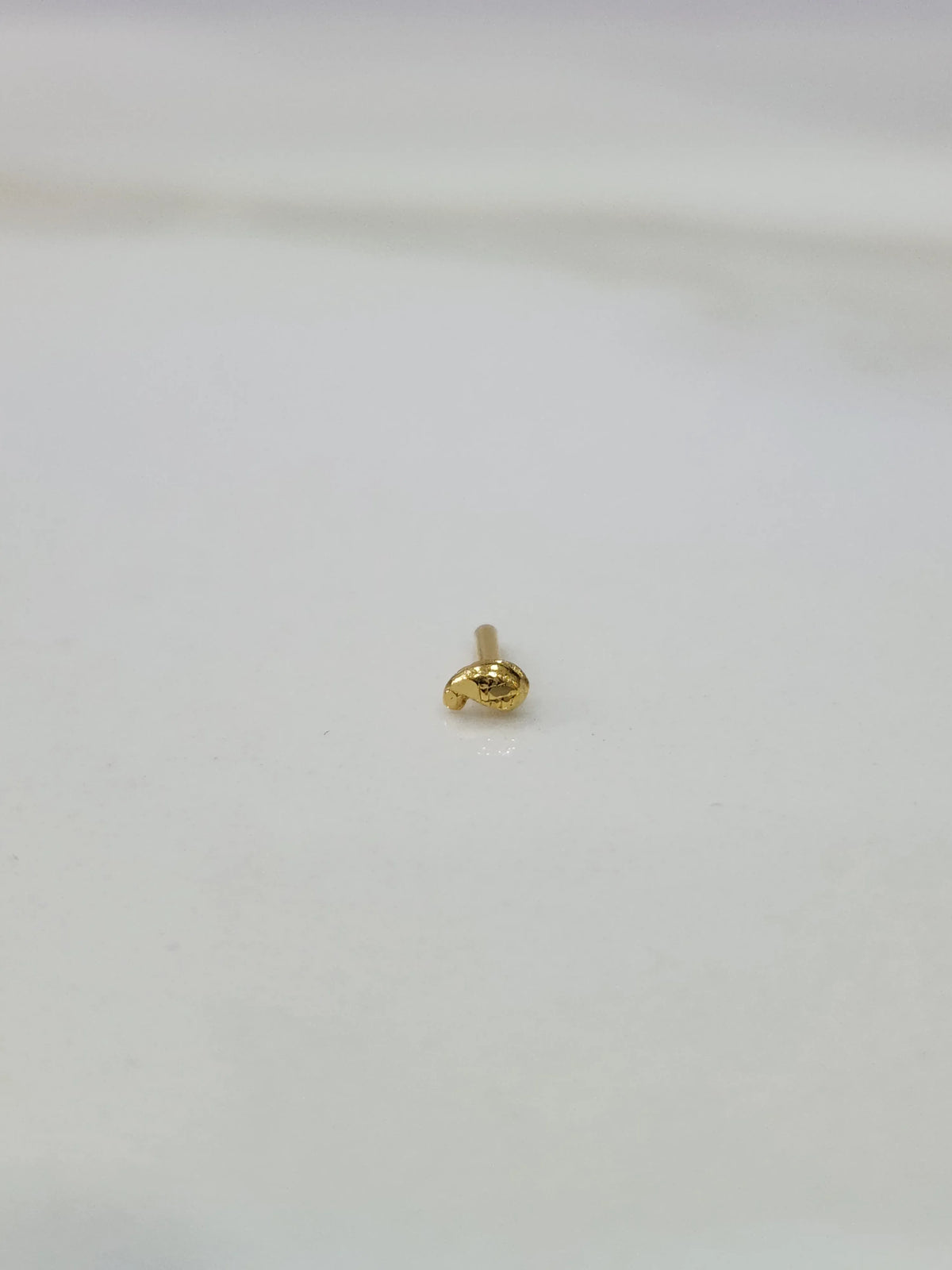 Slight angled view of a tiny 18K gold nose pin on a white surface highlighting its lightweight design and polish