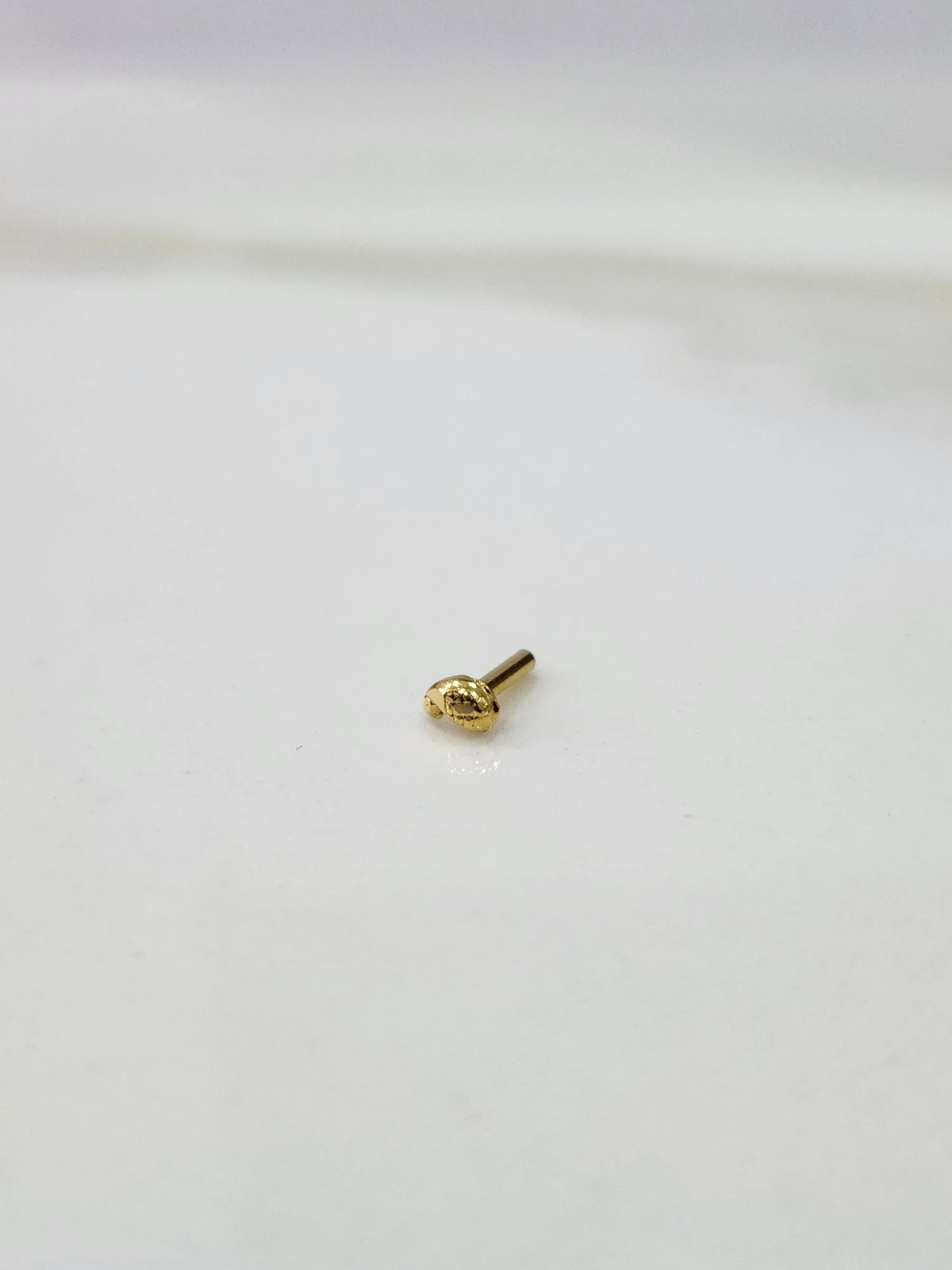 Front view of a small 18K gold nose pin placed on a white background showing its compact size and detailing
