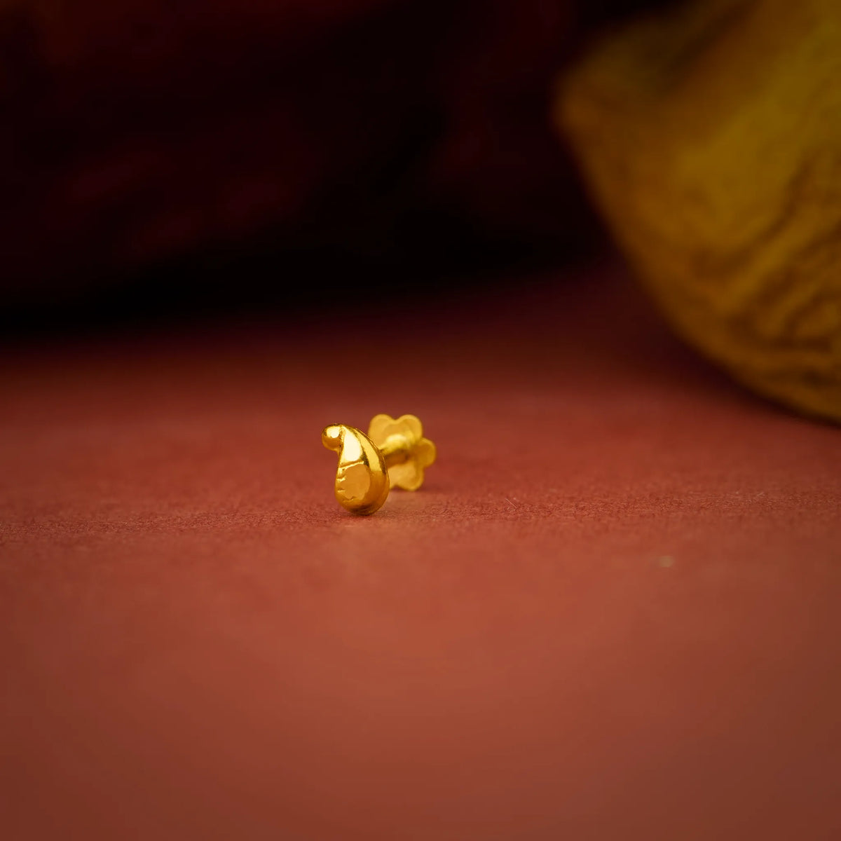 Artistic product shot of a tiny 18K gold nose pin on a warm brown surface emphasizing its subtle shine