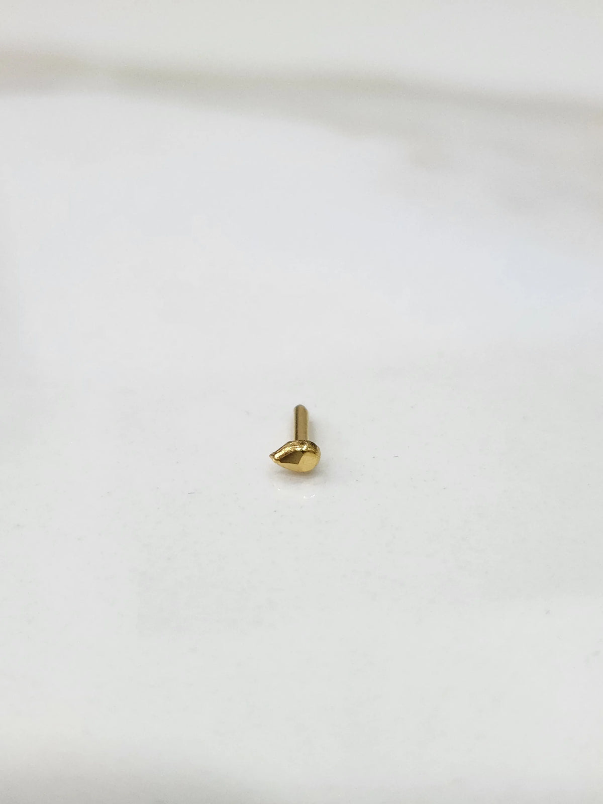 Close up of teardrop gold nose pin placed on white surface showing polished shine