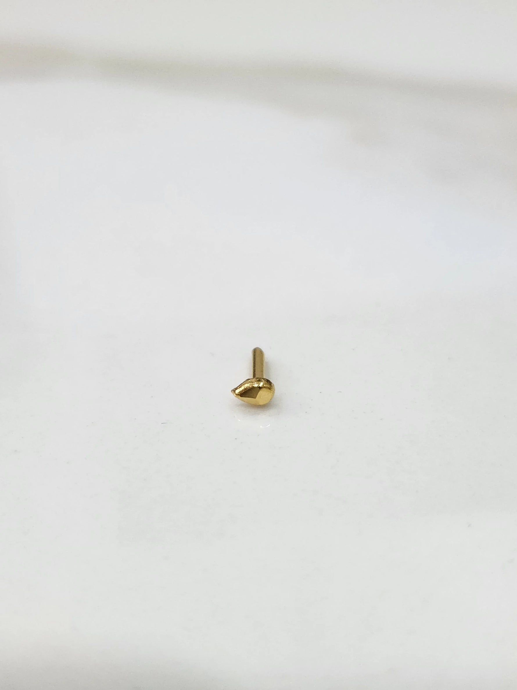 Close up of teardrop gold nose pin placed on white surface showing polished shine