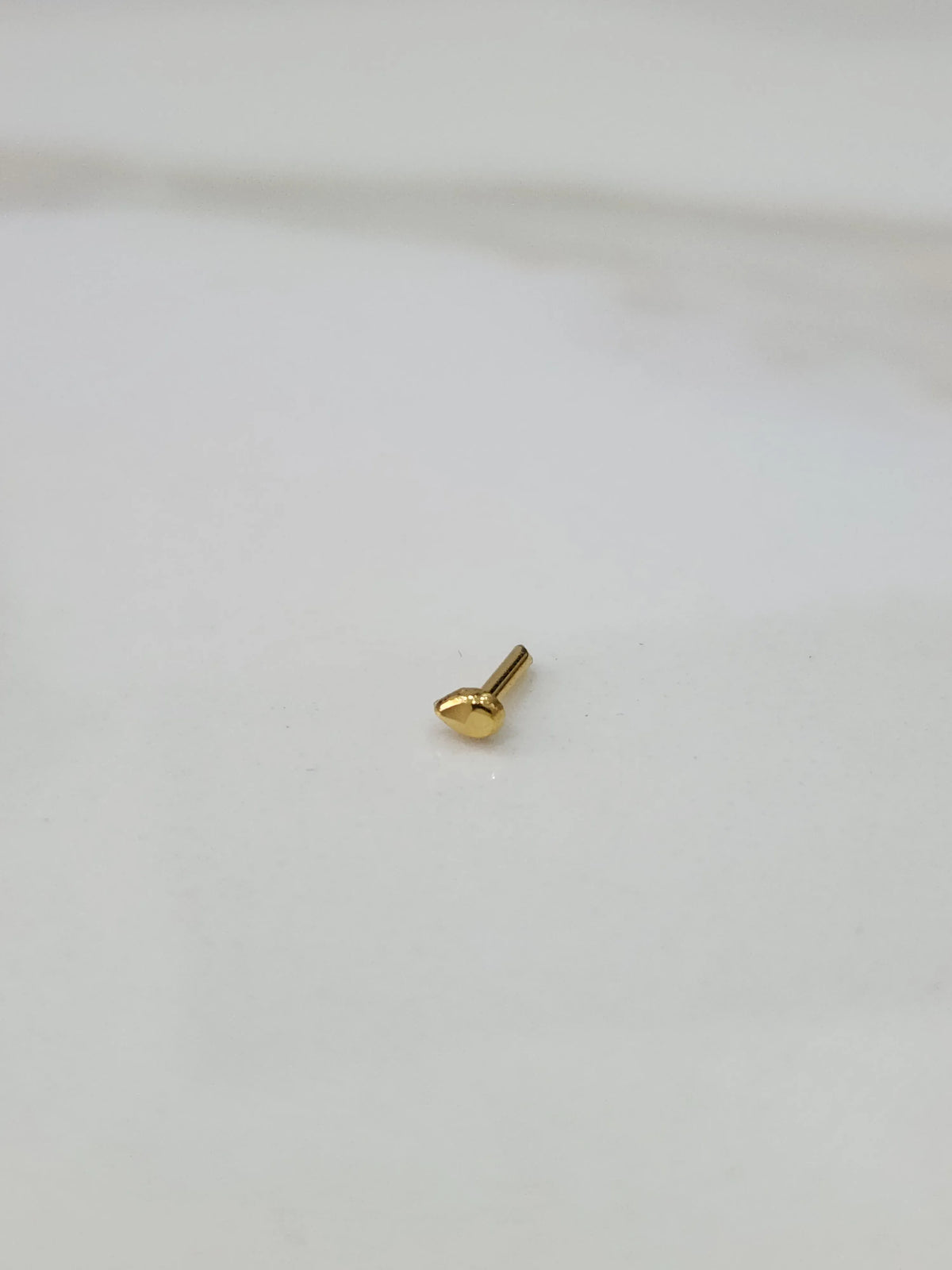 Side angle view of small teardrop gold nose pin highlighting compact and refined design