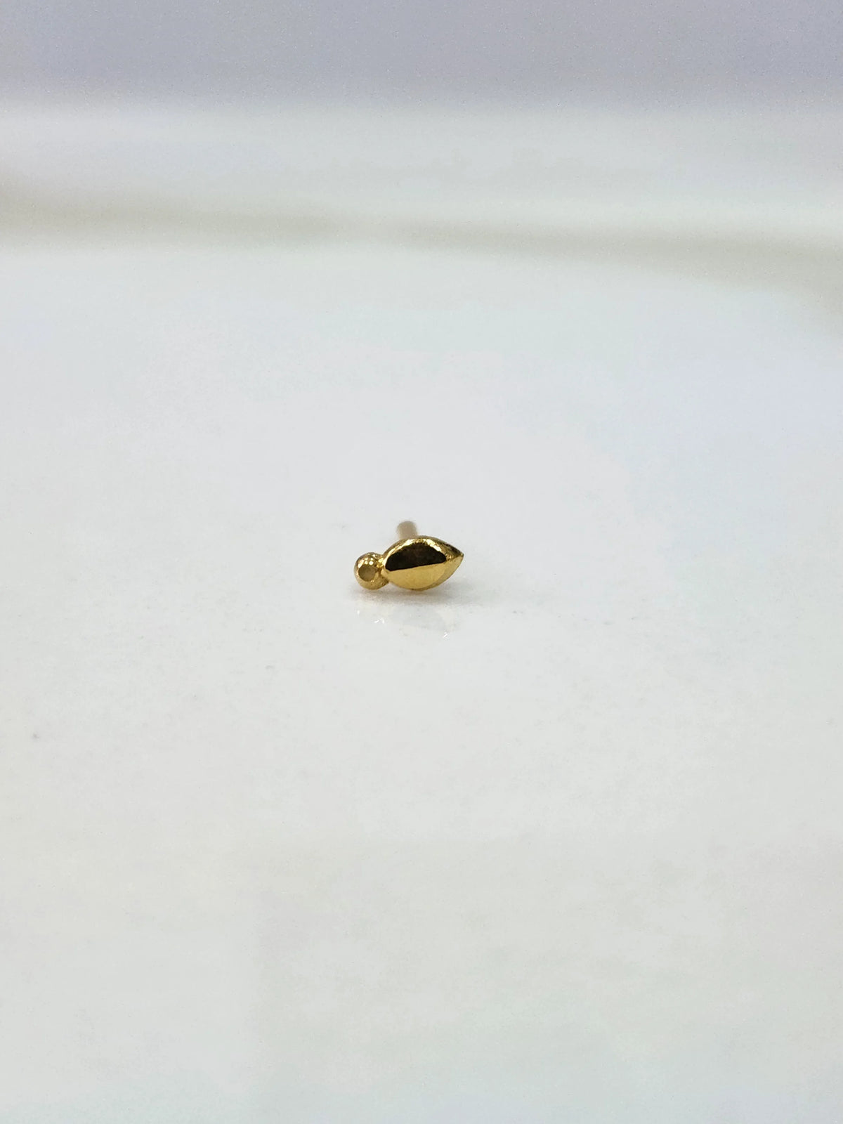 Side view of a lightweight gold nose pin on a white surface showing its compact size and fine detailing