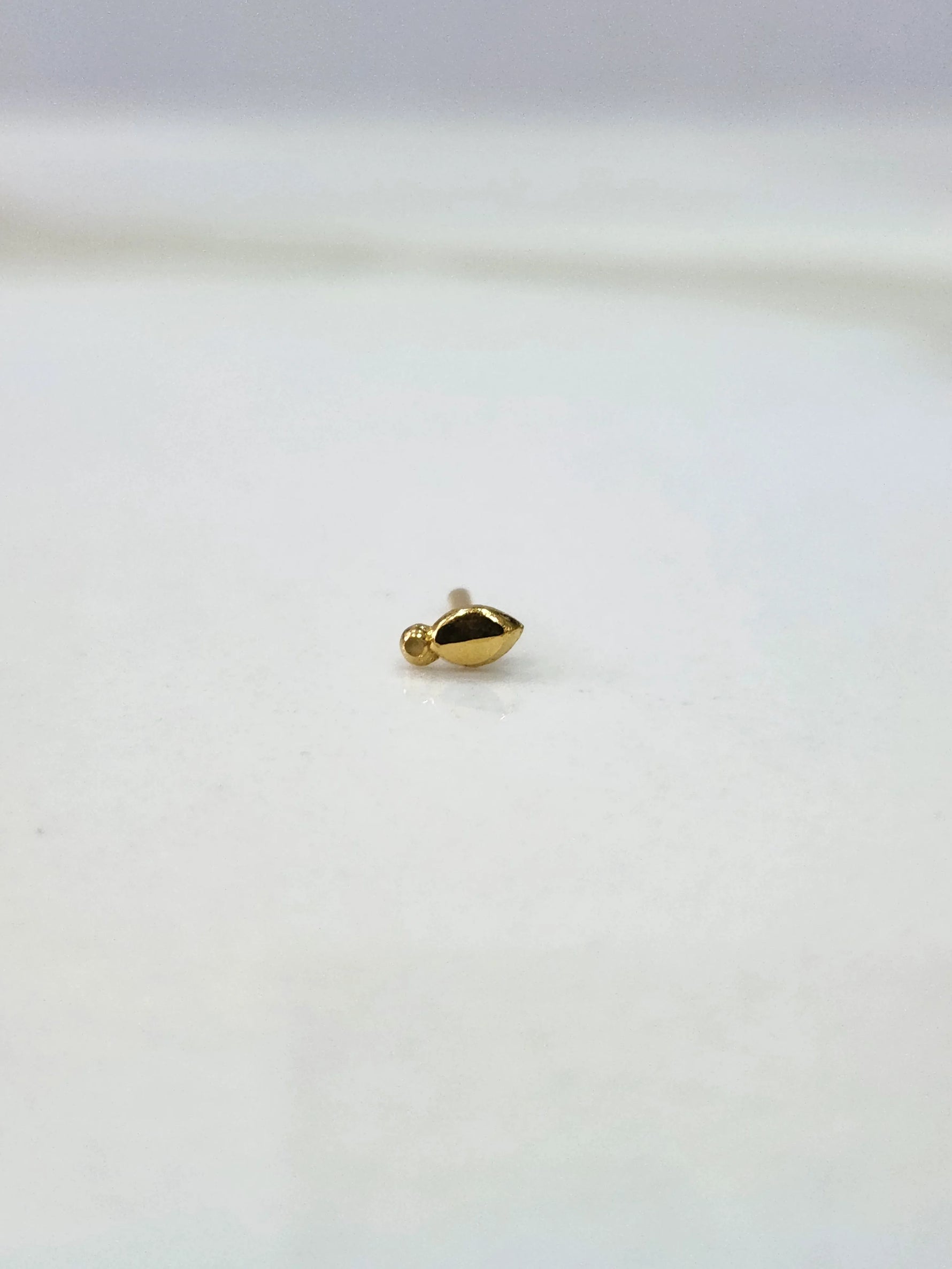 Side view of a lightweight gold nose pin on a white surface showing its compact size and fine detailing