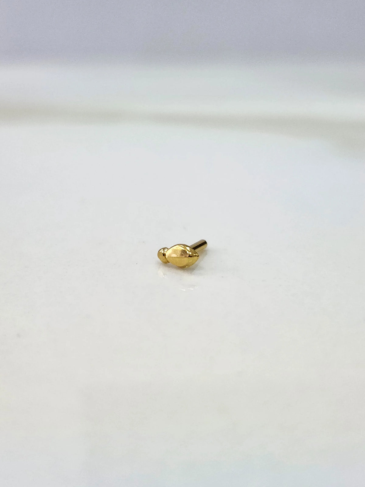 Front view of a small gold nose pin on a white background emphasizing its delicate design