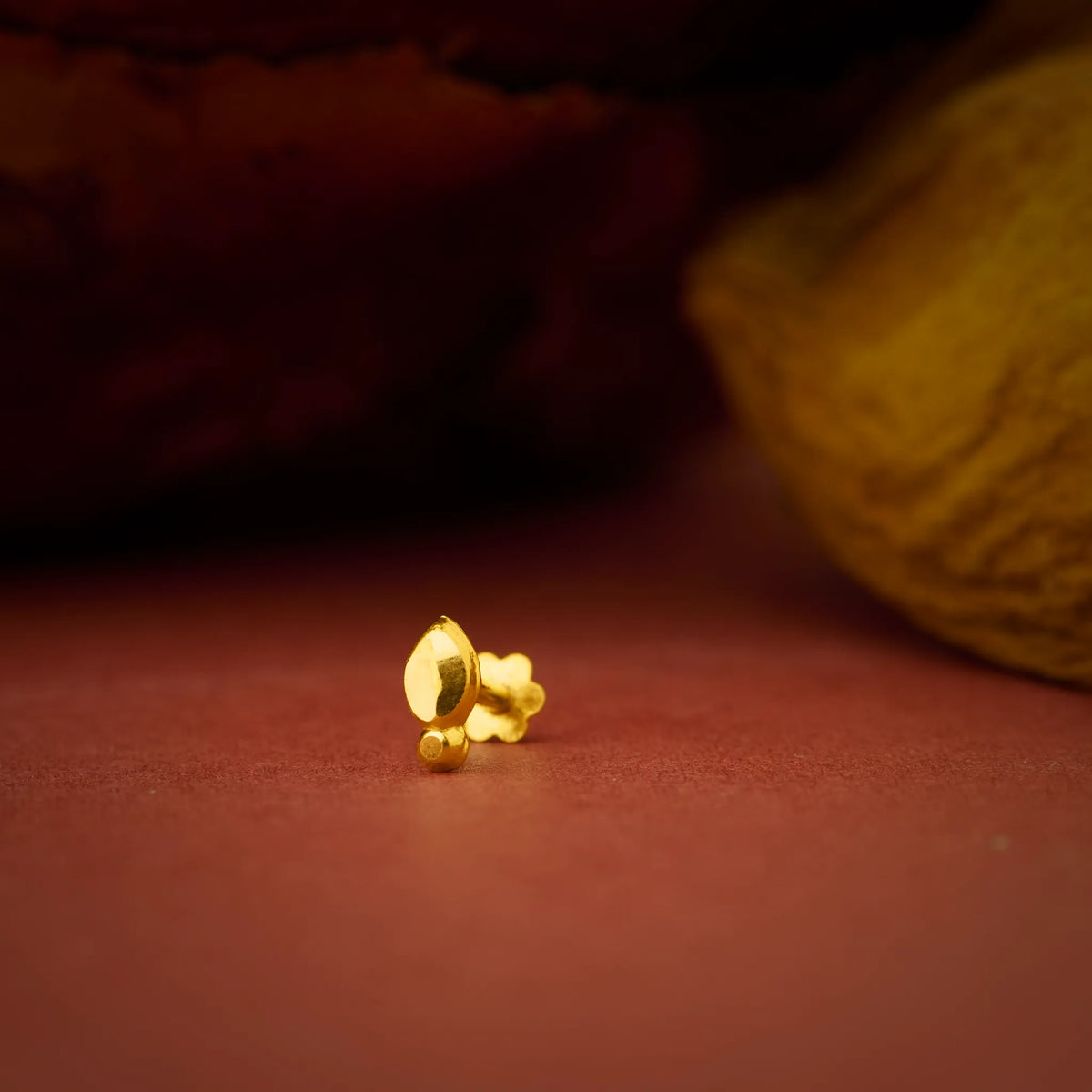 Artistic close up of a gold nose pin placed on a warm textured surface highlighting its polished finish