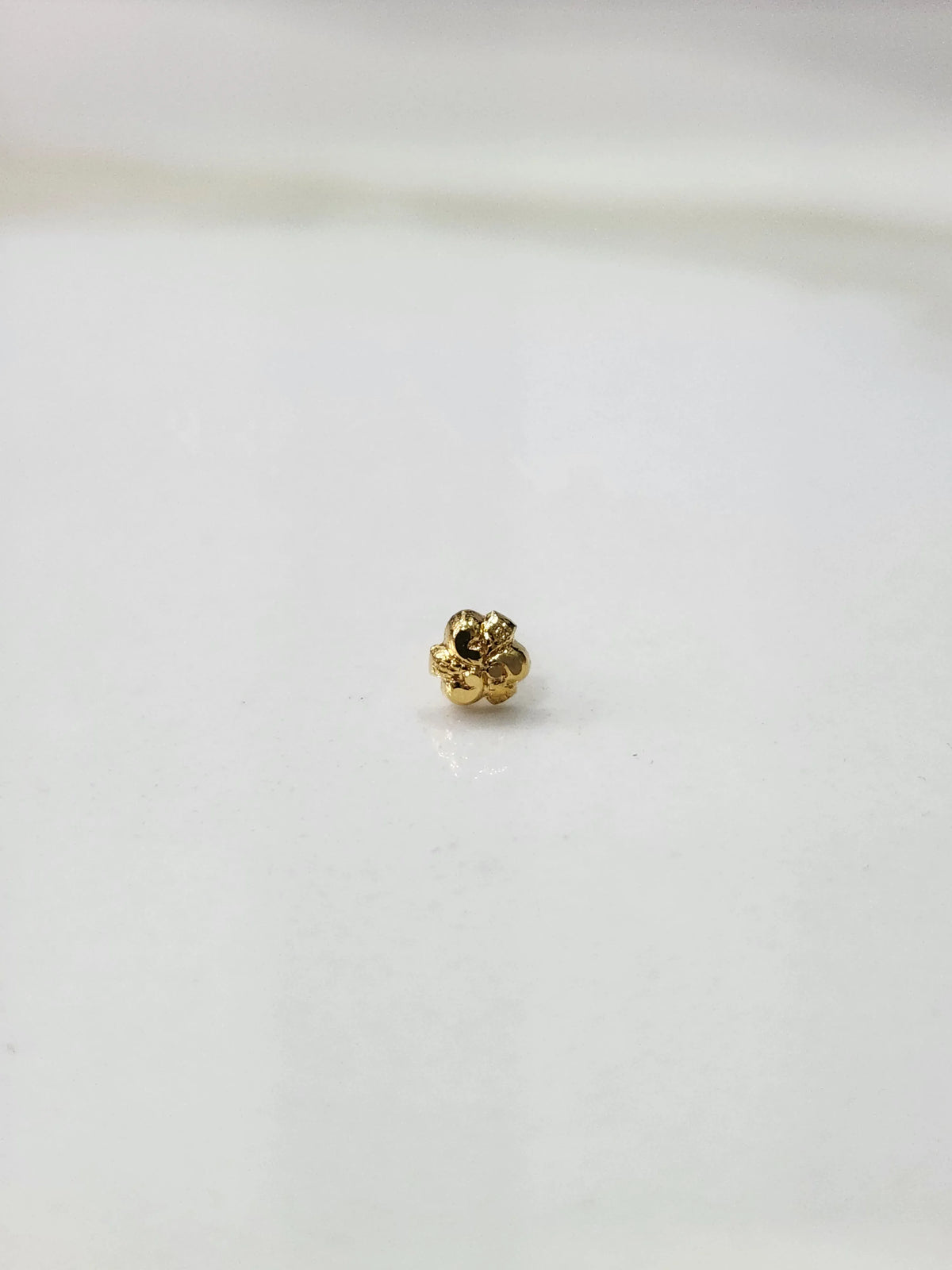 Side view of a delicate gold nose pin on a white surface emphasizing fine craftsmanship and subtle shine
