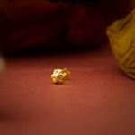 Close up of a gold nose pin placed on a warm red surface highlighting its polished finish and intricate detailing