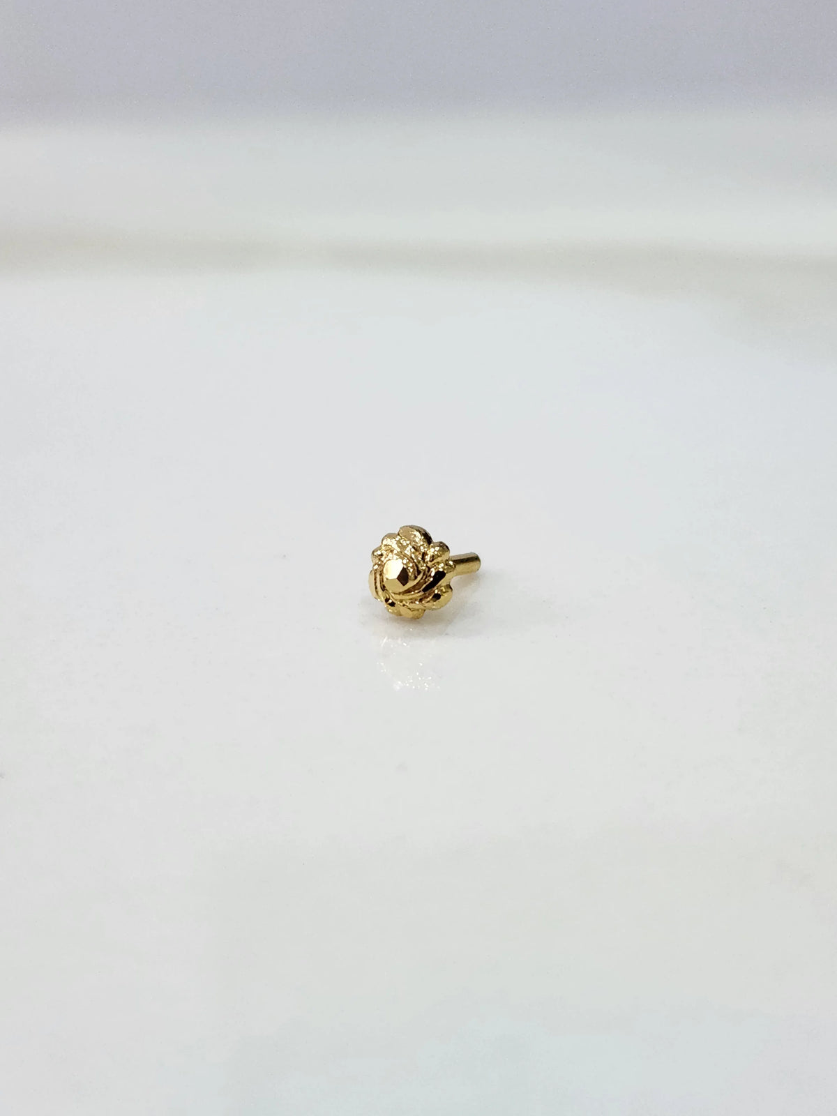 Front view of a tiny gold nose pin on a white background displaying its compact size