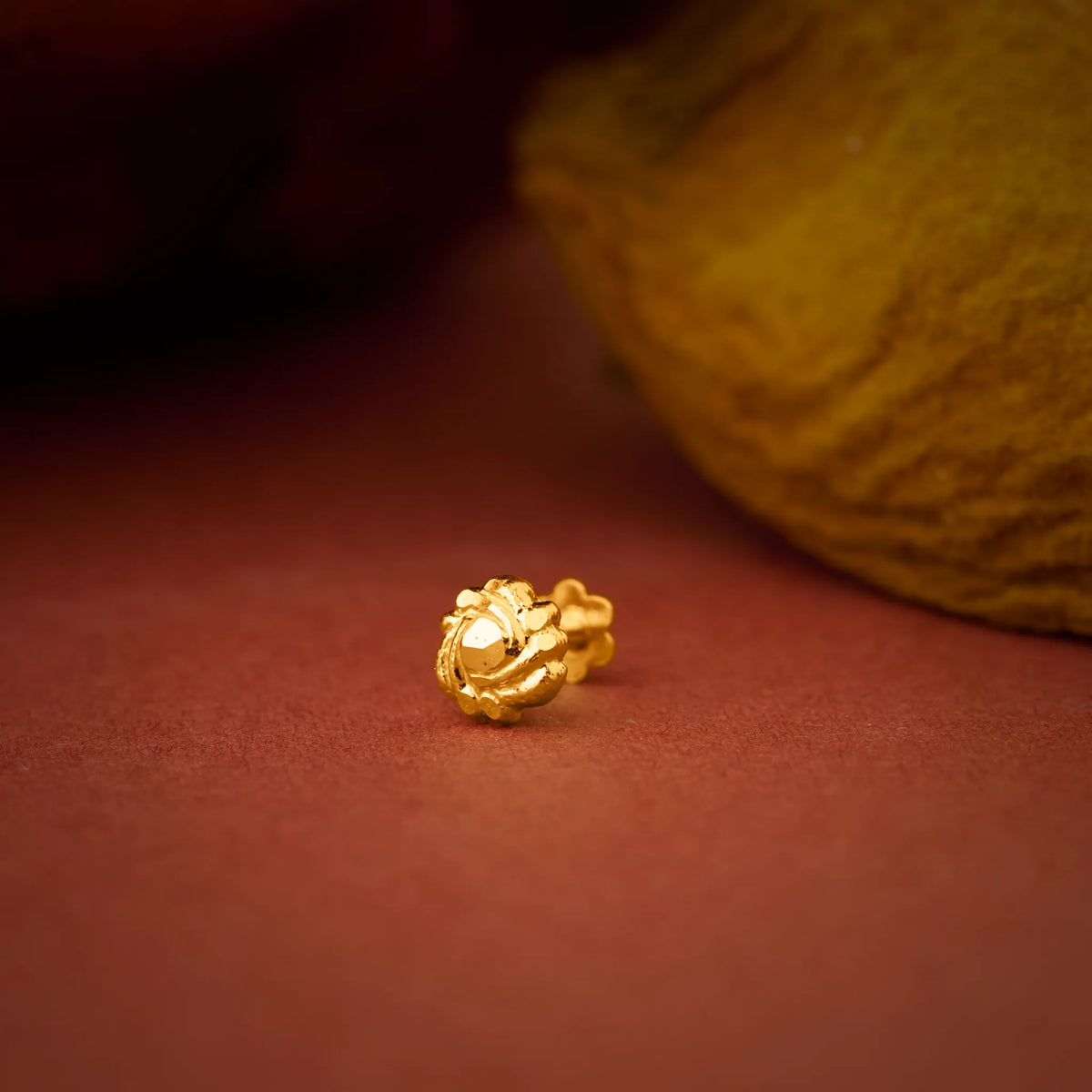 Close up of a gold nose pin placed on a warm textured surface highlighting its polished finish and intricate detailing