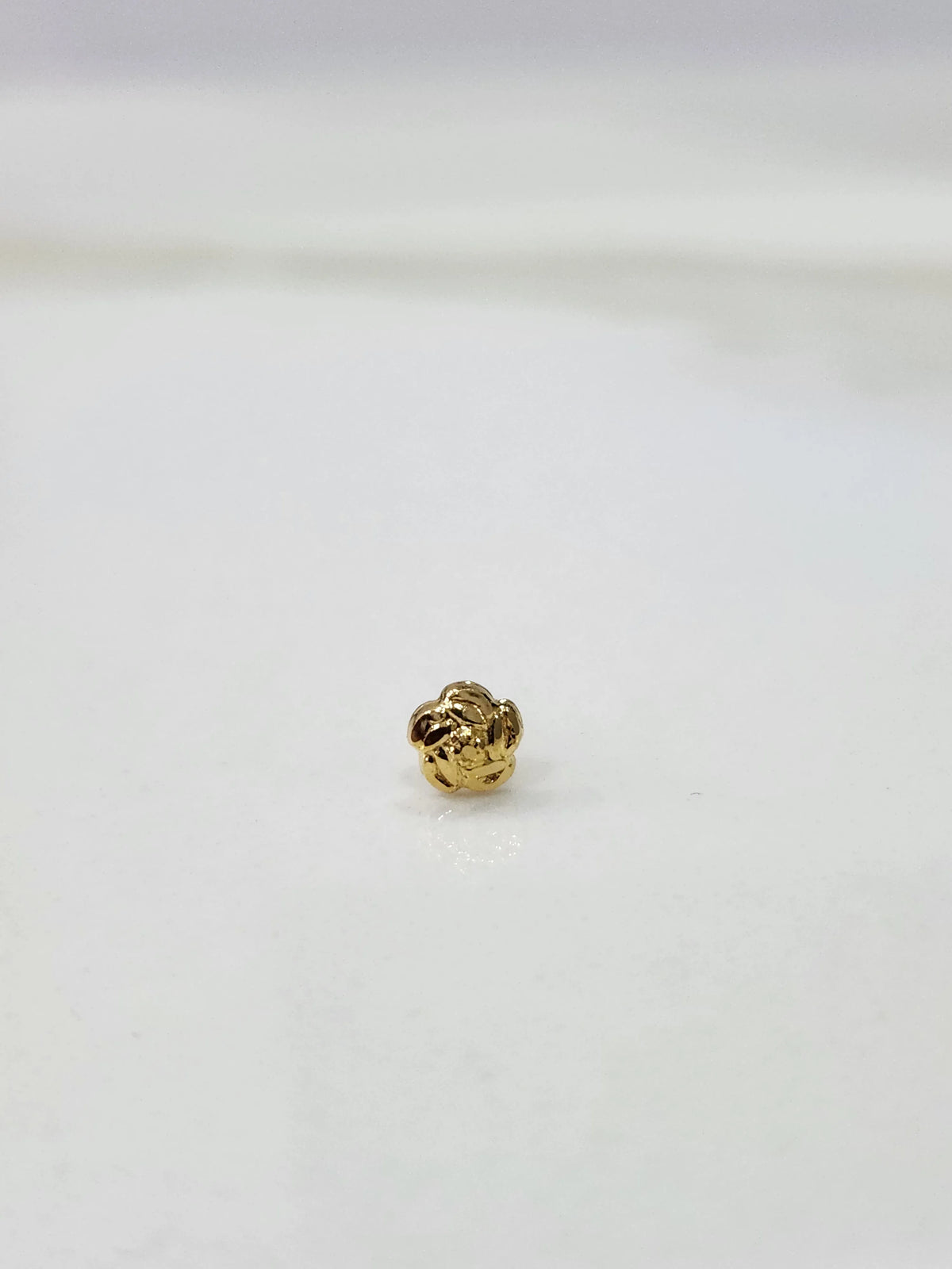 Side view of a tiny gold nose pin on a white surface displaying its lightweight build and subtle shine