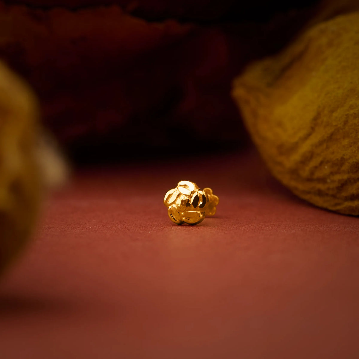 Close up of a gold nose pin placed on a warm brown surface with textured background highlighting its polished finish
