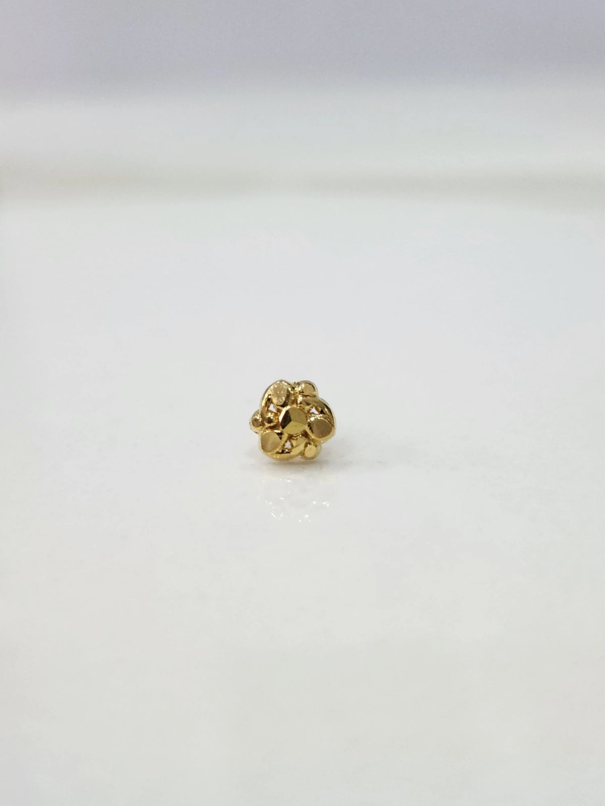 Slight side view of the gold nose pin on a white surface highlighting its lightweight and delicate design