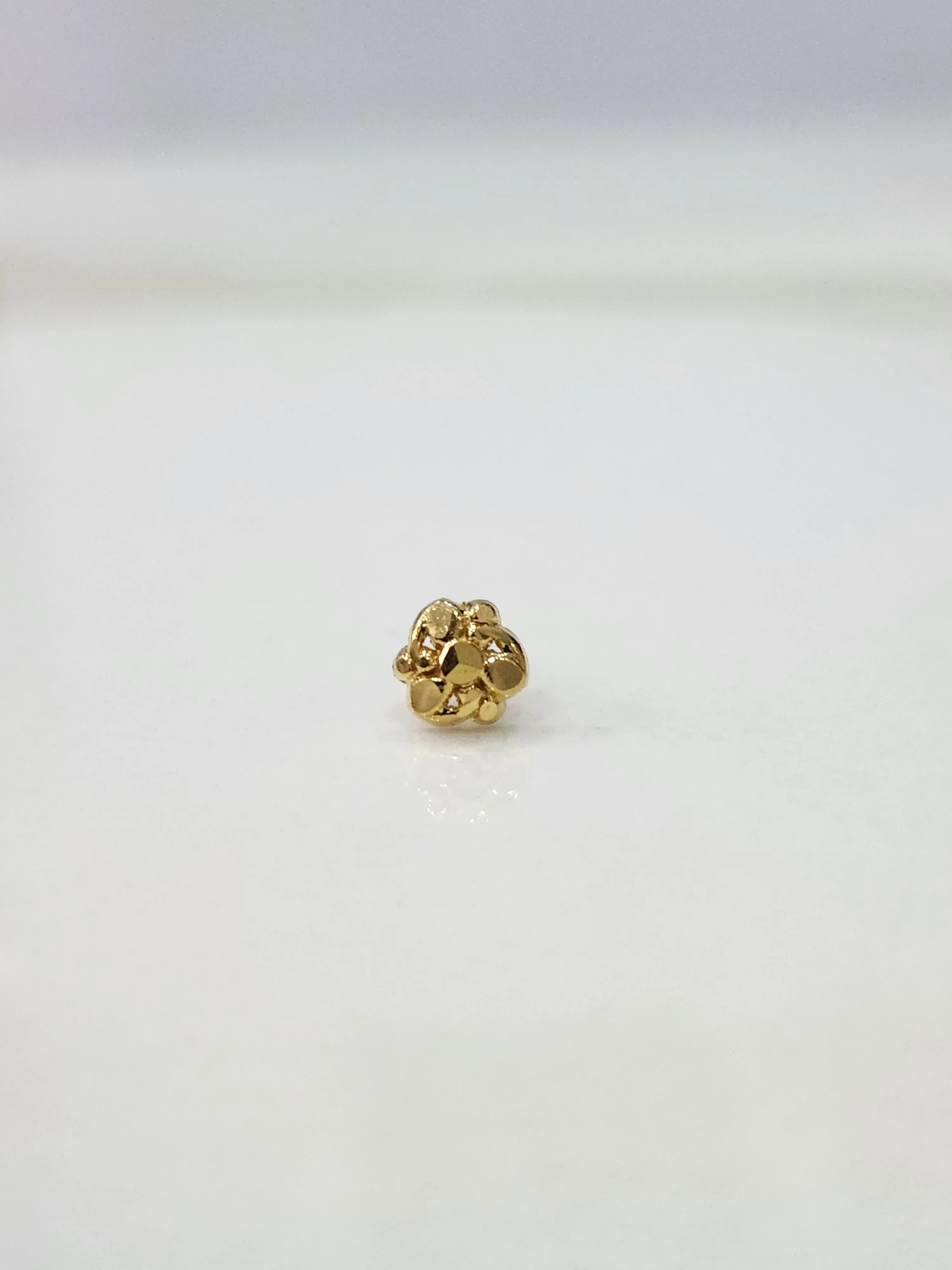 Slight side view of the gold nose pin on a white surface highlighting its lightweight and delicate design