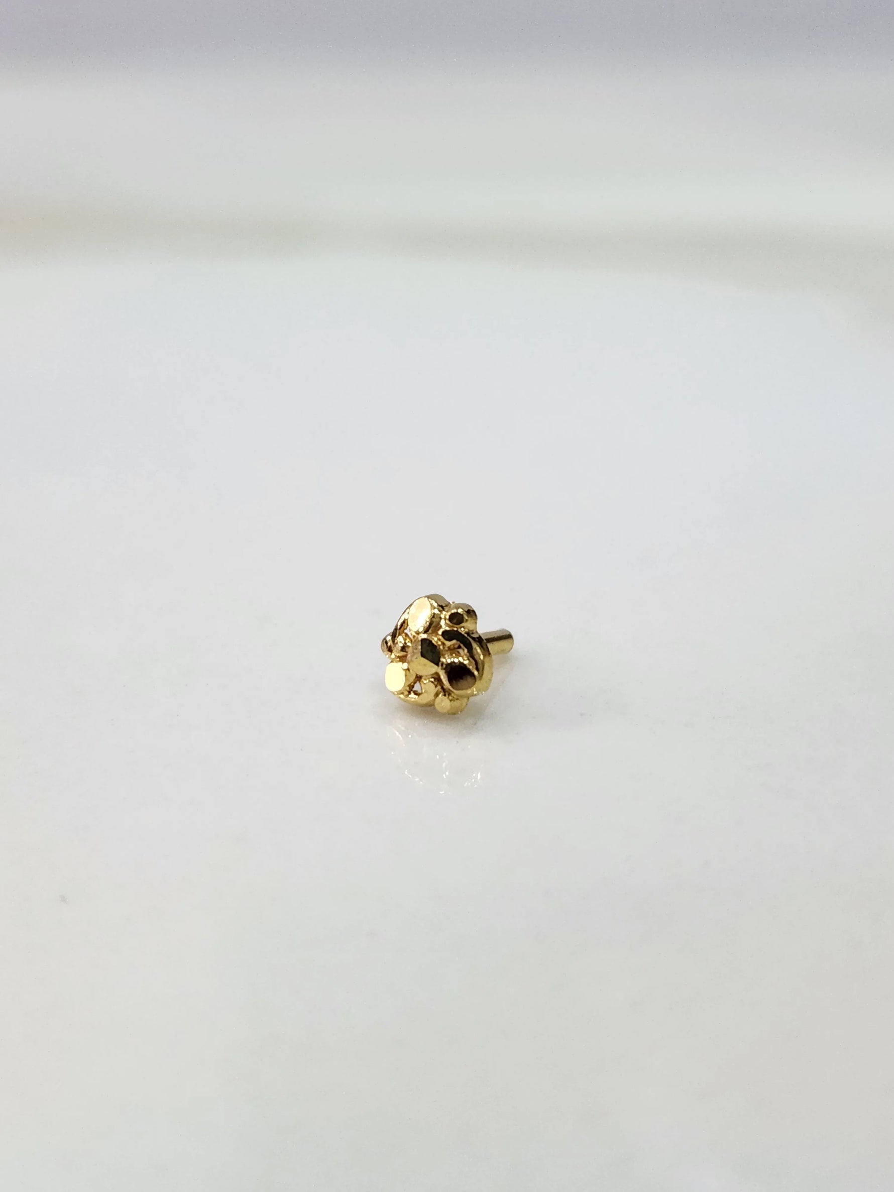 Front view of a tiny gold nose pin on a white background showing its compact size and fine detailing