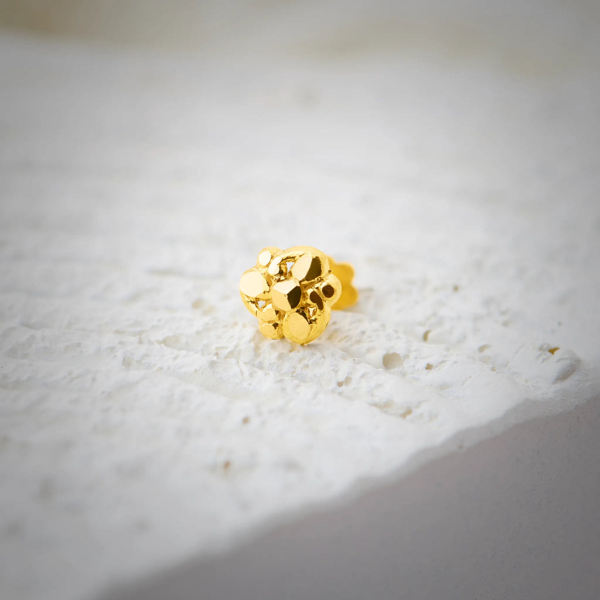 Close up view of a small gold nose pin placed on a textured white surface highlighting its polished finish