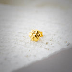 Close up view of a small gold nose pin placed on a textured white surface highlighting its polished finish