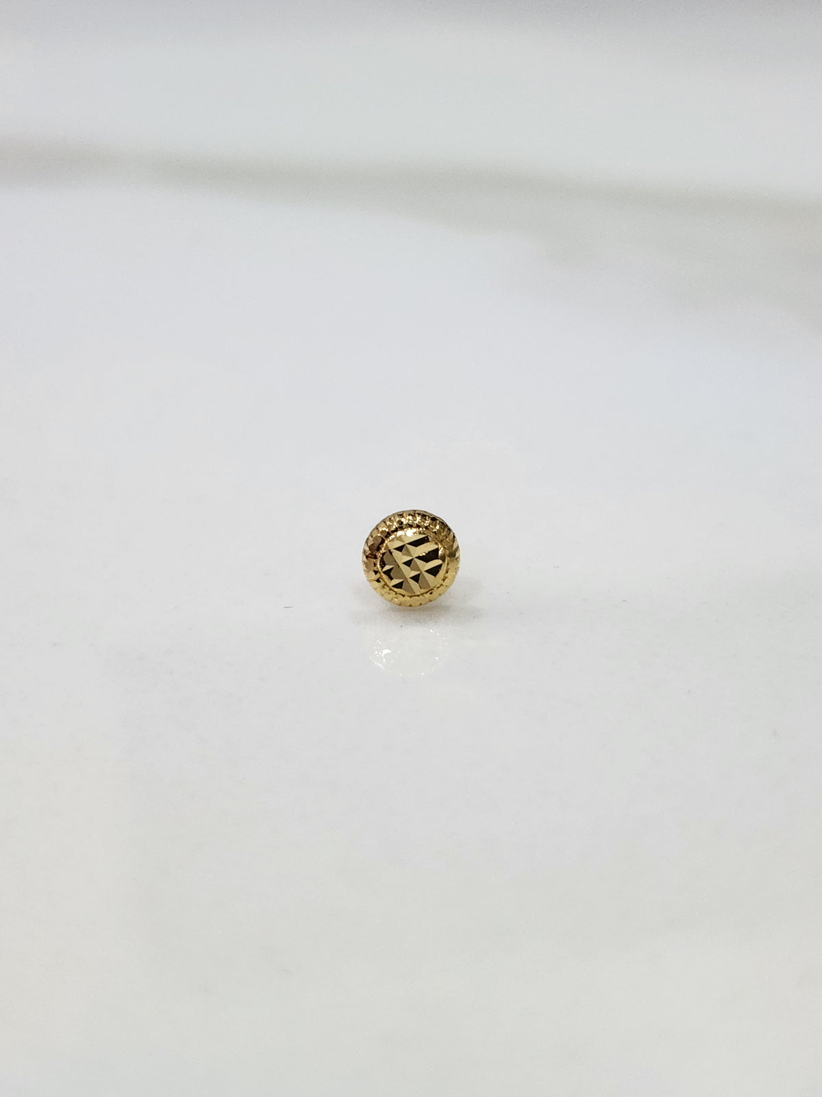 Close up of round textured gold nose pin design on white background elegant and refined for women