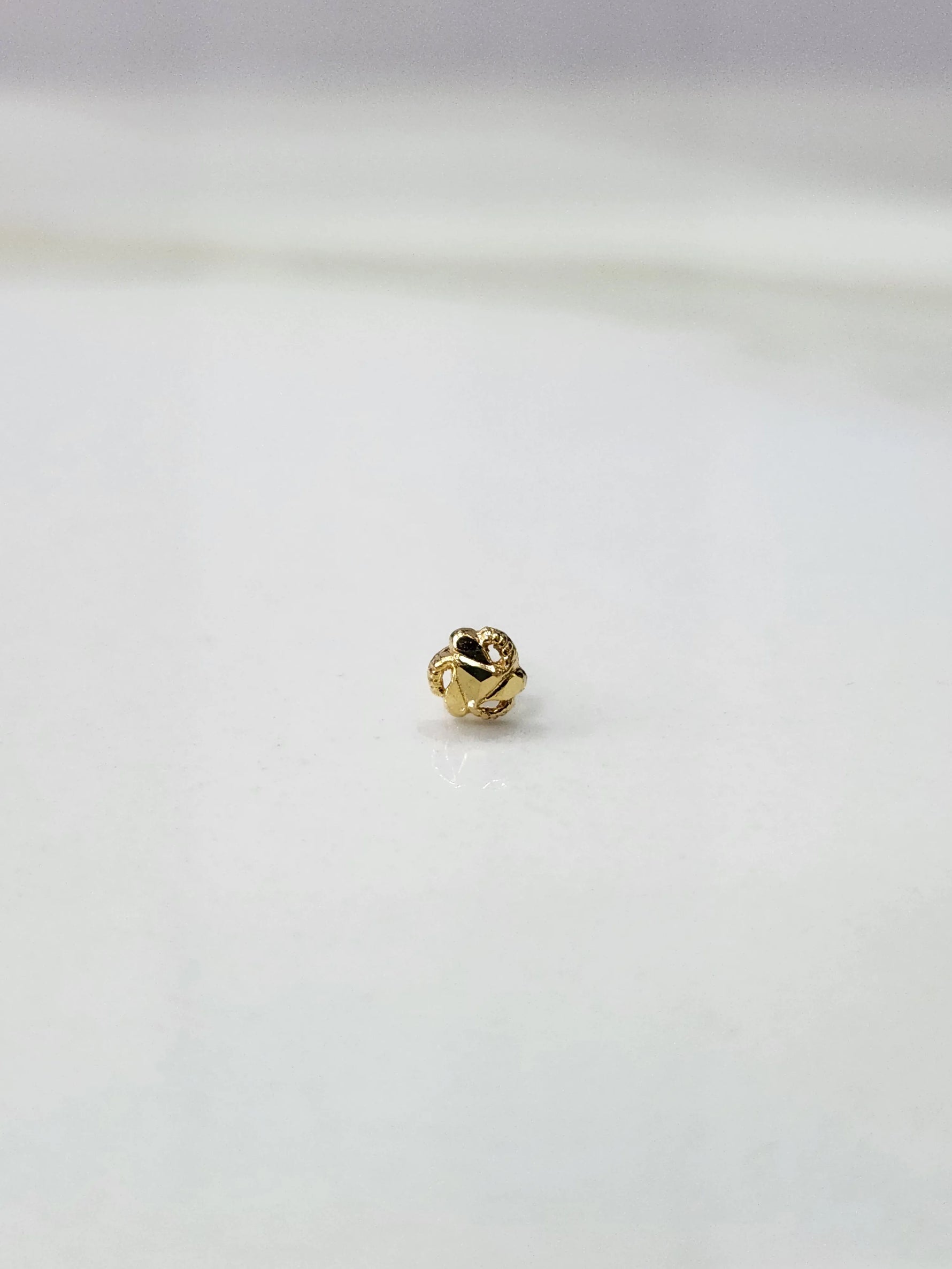 Side view of a small gold nose pin on a white surface showing its post length and polished finish