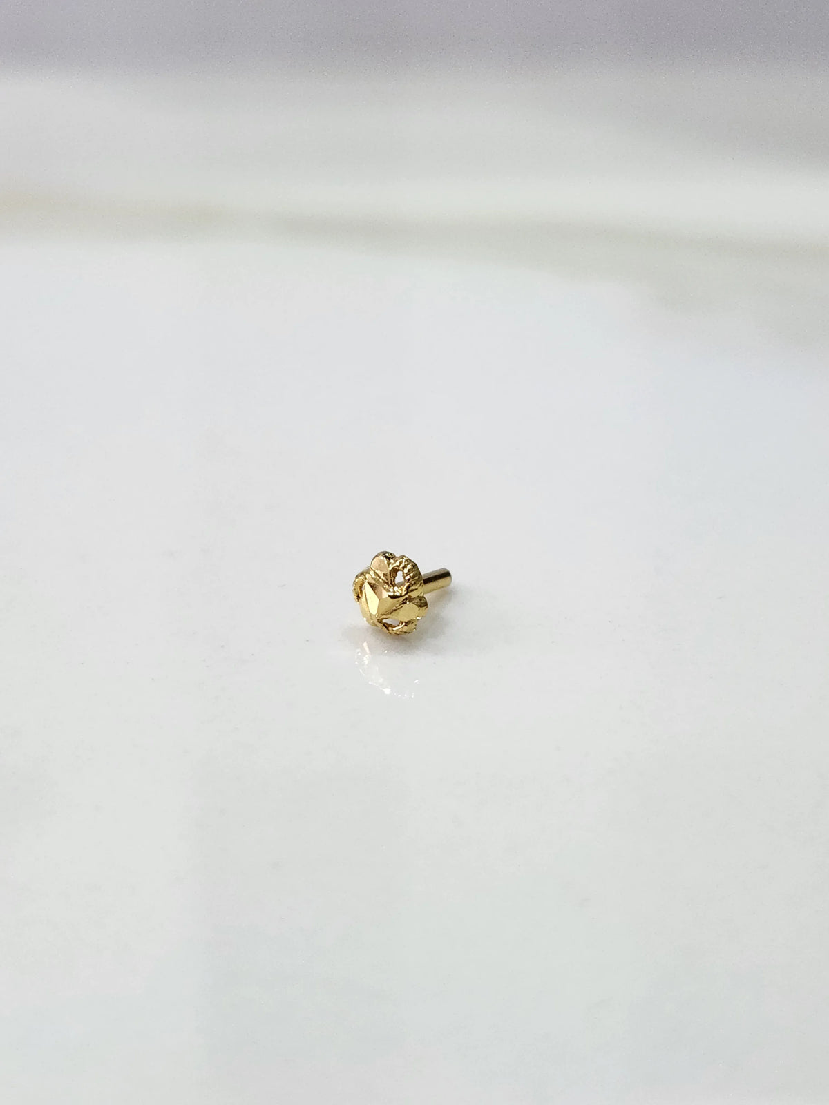 Front view of a miniature gold nose pin placed on a white background highlighting compact design
