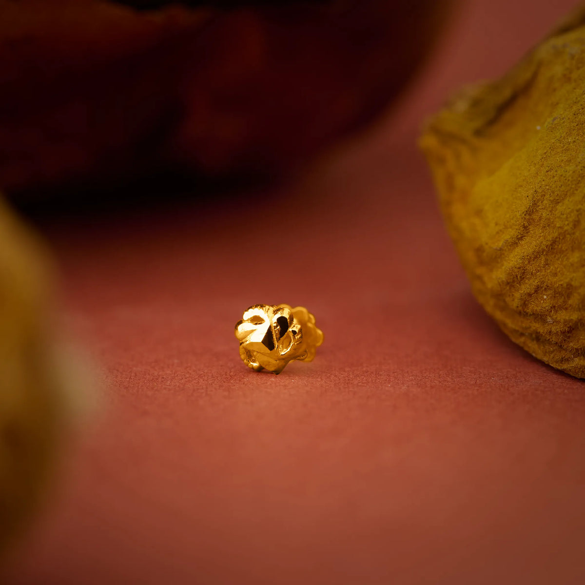 Close up of a small floral gold nose pin placed on a warm terracotta surface highlighting its intricate carved detailing
