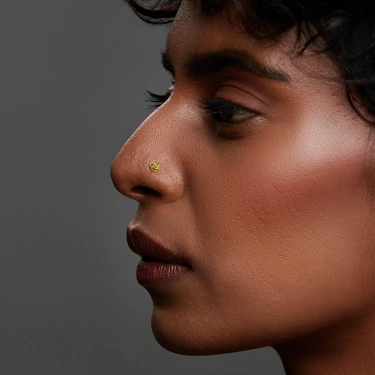 Side profile of a woman wearing a delicate gold nose pin showcasing a refined modern look