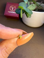 Hand holding a tiny gold nose pin near a Yuvora box to show its lightweight and wearable size